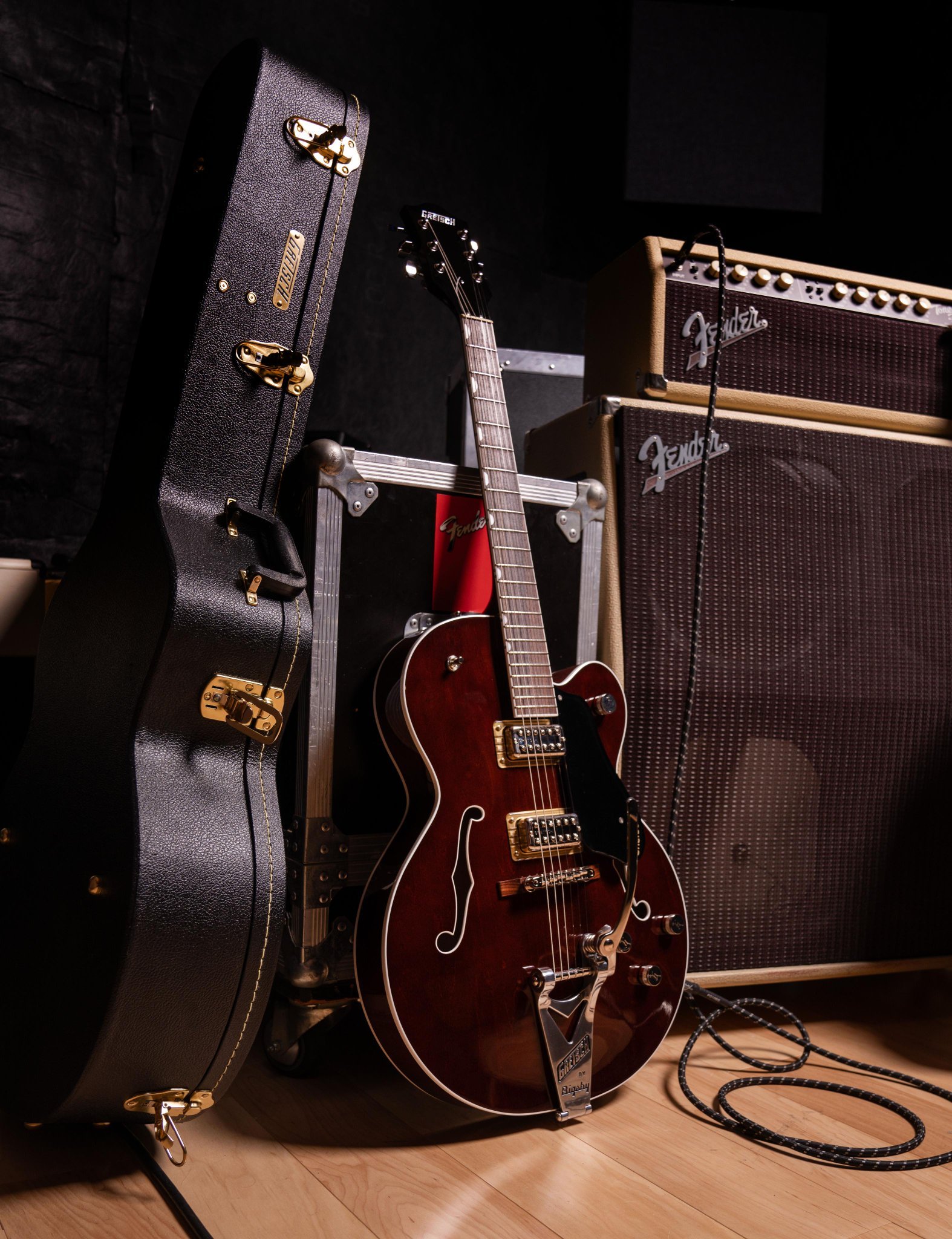 Electric guitar with a hard case, two Fender amplifiers, and audio cable in a studio setting.