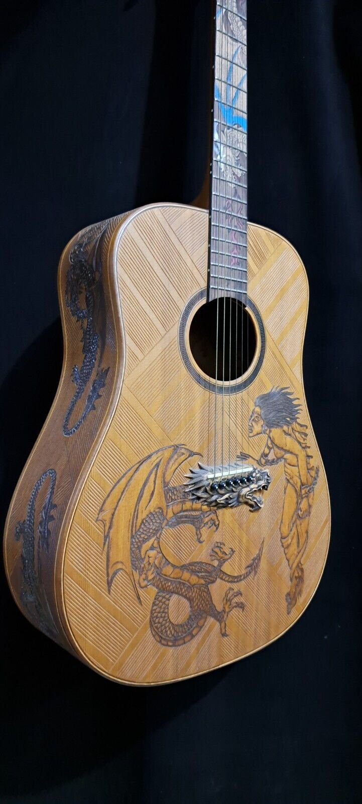 Acoustic guitar with intricate dragon and warrior engravings on a wooden body, set against a dark background.