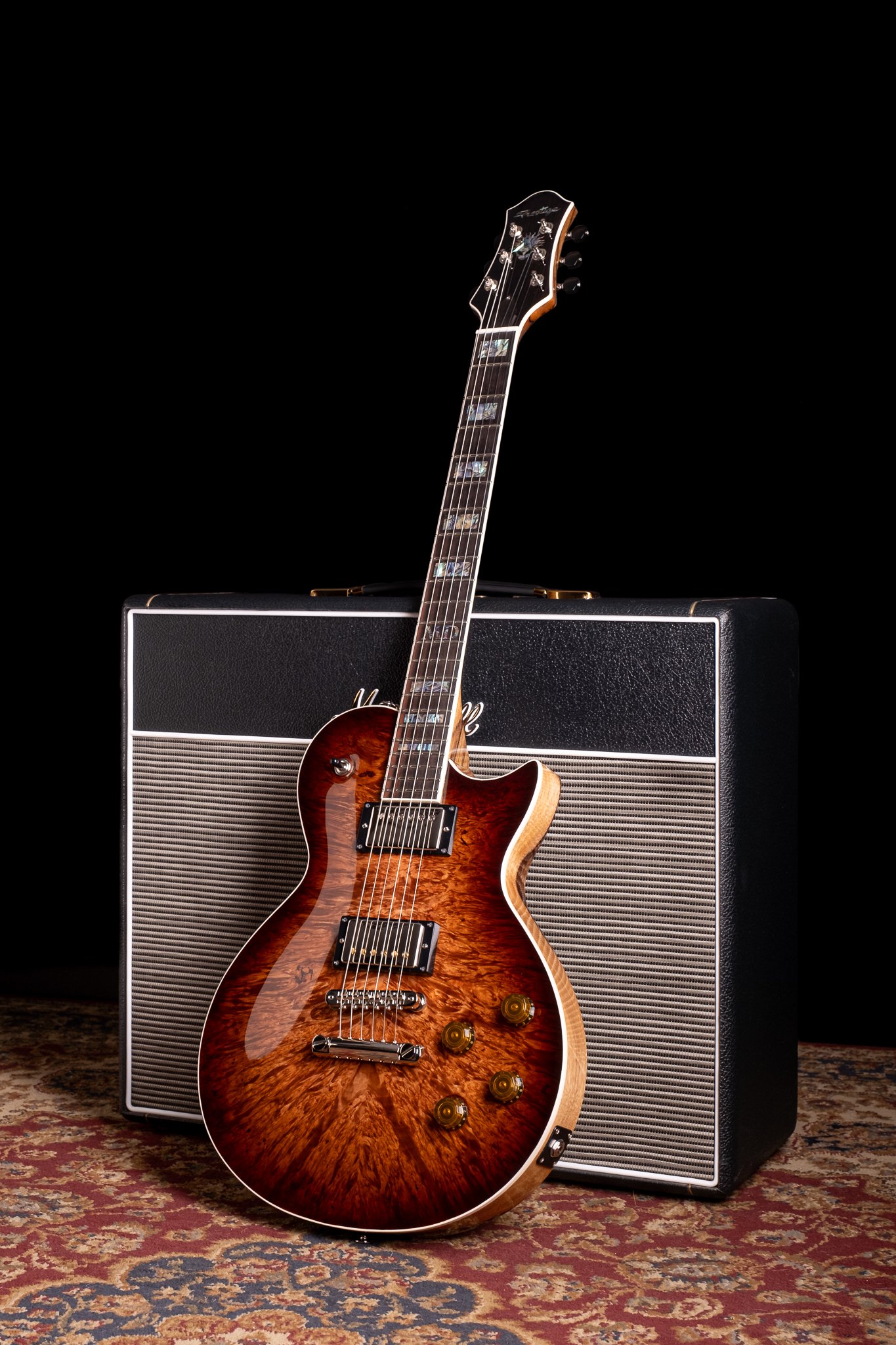 Electric guitar with a flame maple top leaning against a Marshall amplifier on a patterned rug.