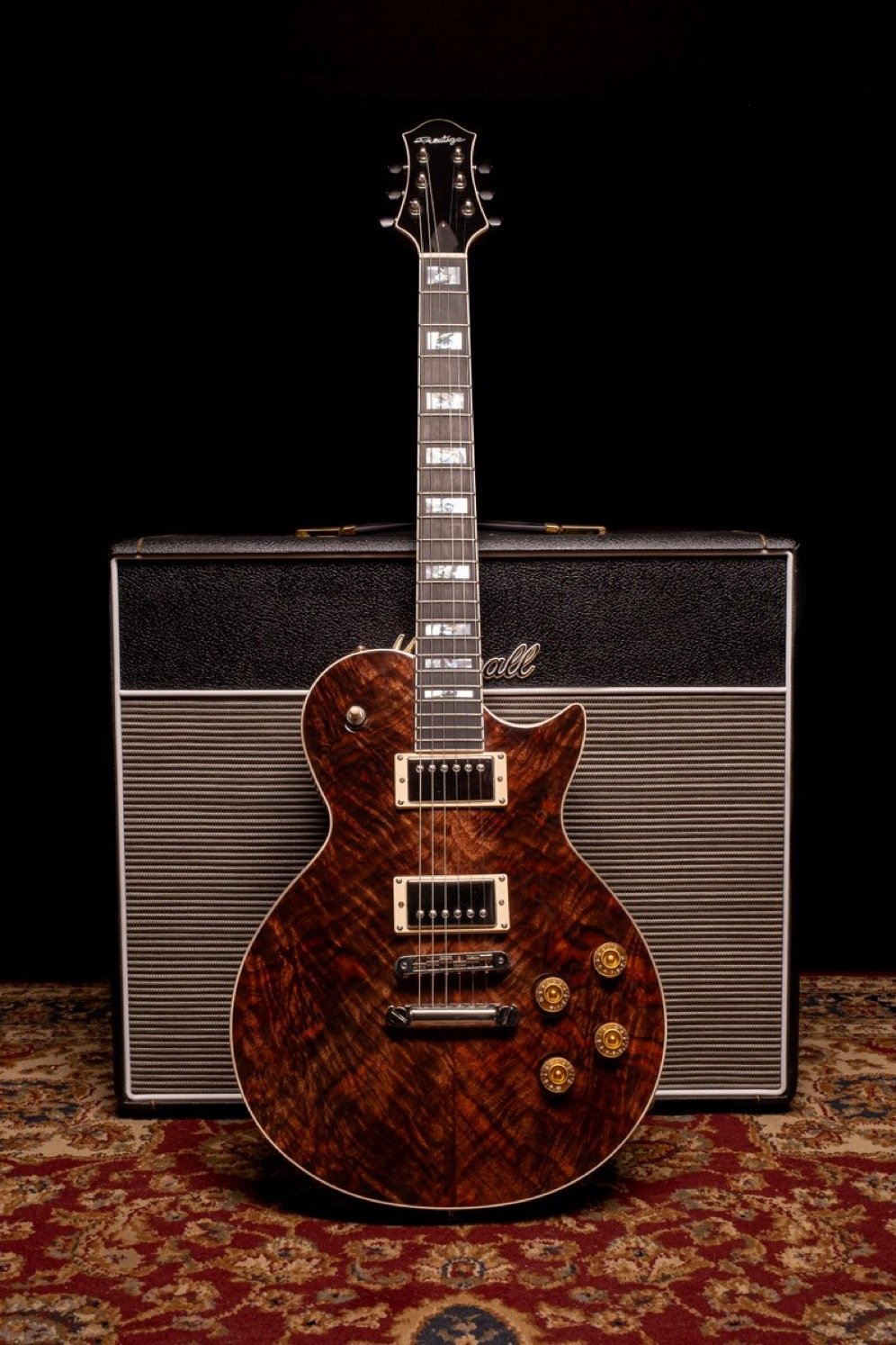 Electric guitar with a dark wood finish in front of a Marshall amplifier on a patterned carpet.