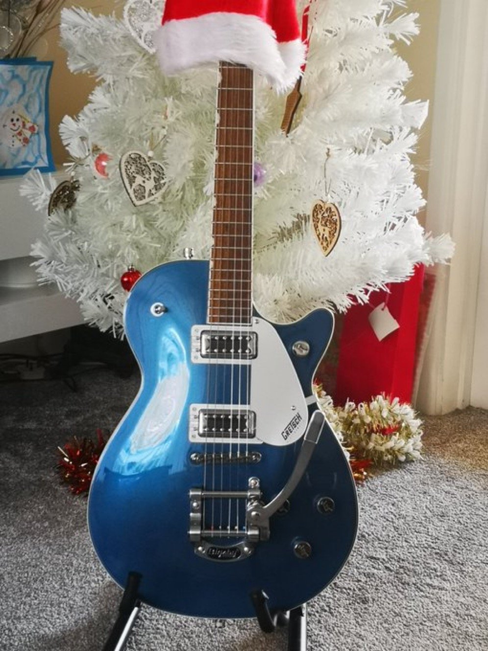 Blue electric guitar on stand in front of a white Christmas tree