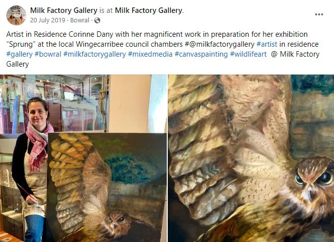 Artist in residence displaying a large owl painting at Milk Factory Gallery.