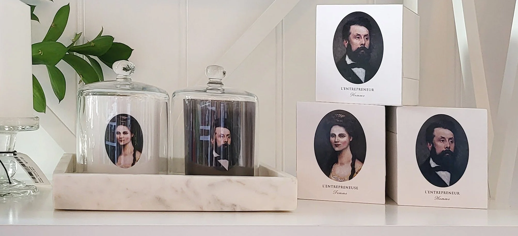 Display of decorative candles and boxes featuring vintage portraits, with a green plant in the background.