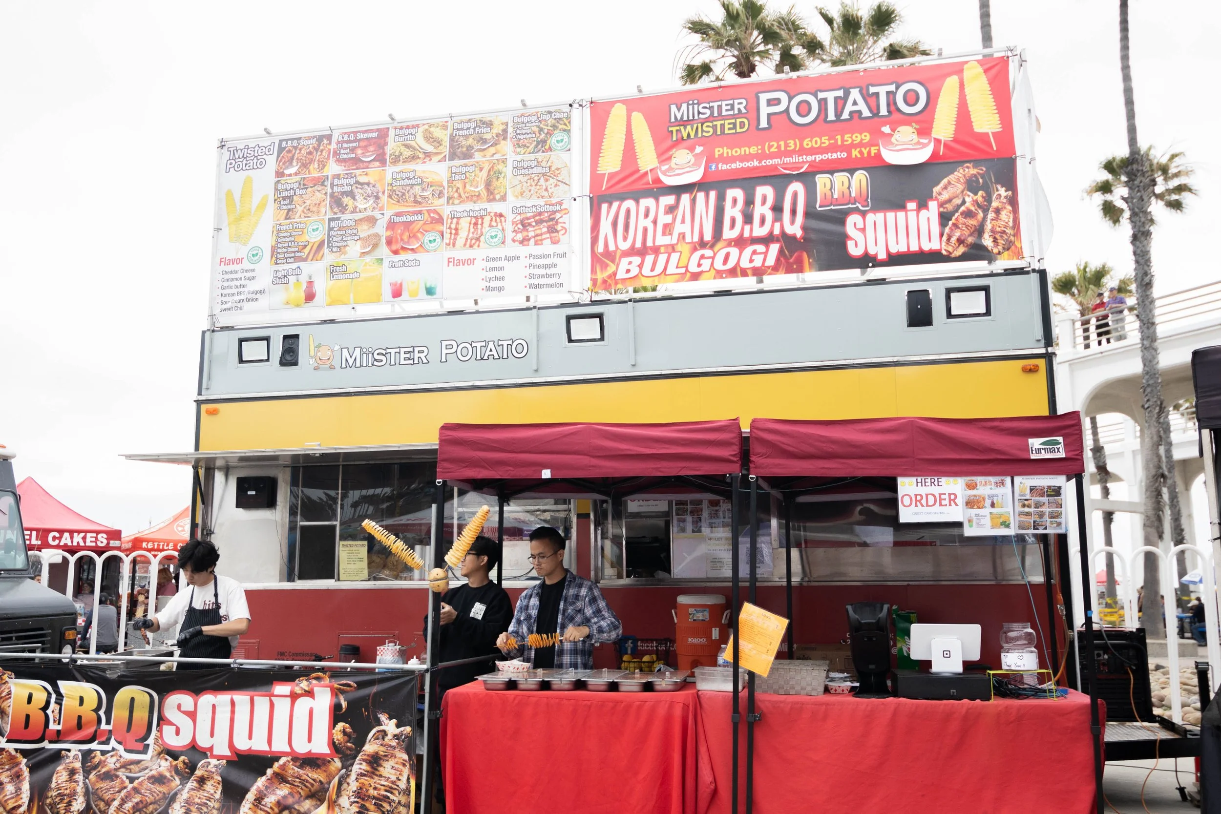 Food truck named 'Mister Potato' selling Korean BBQ, squid, and twisted potatoes at an outdoor event with palm trees in the background.