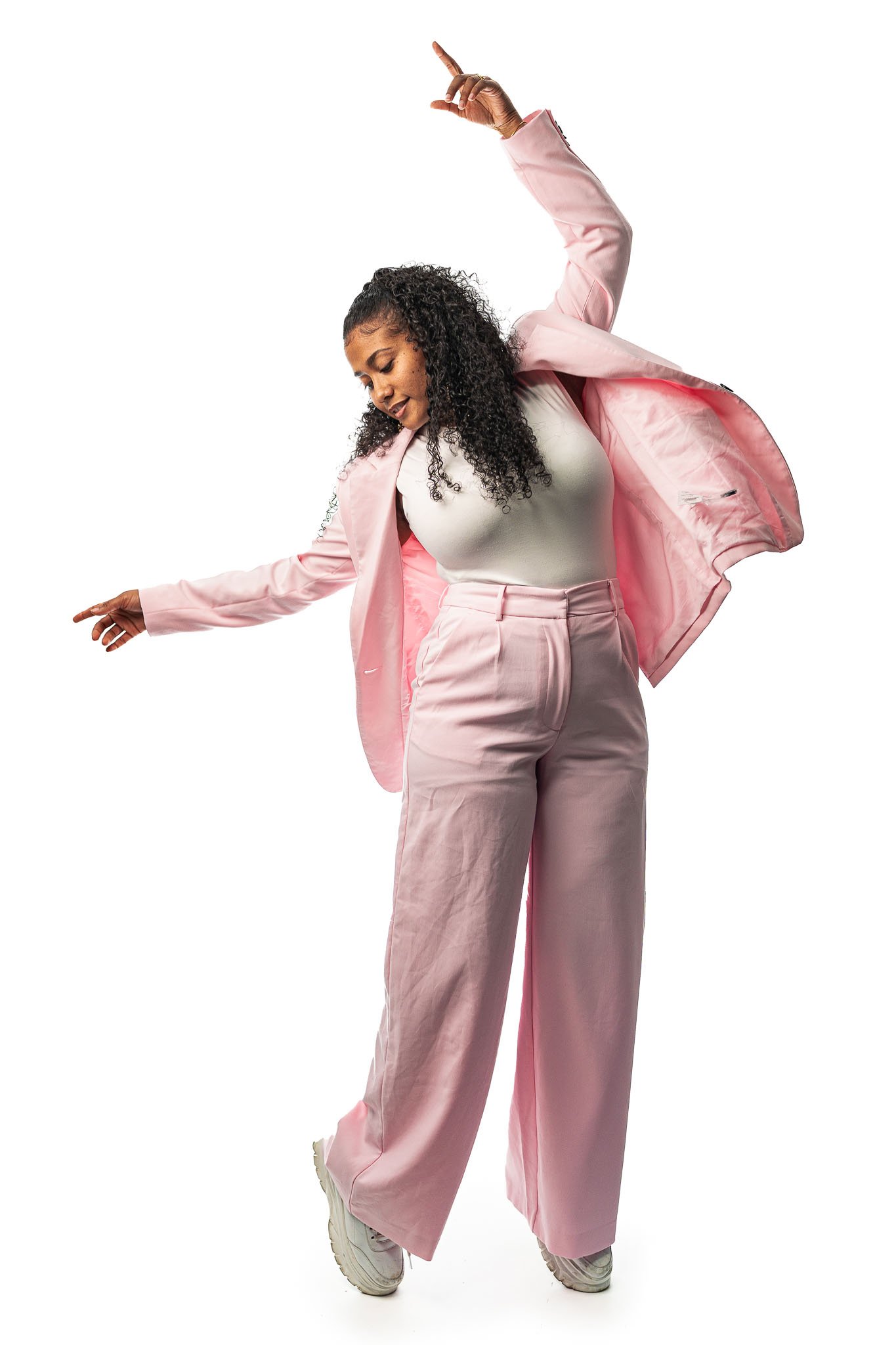 Vrouw in een lichtroze pak danst tegen een witte achtergrond.