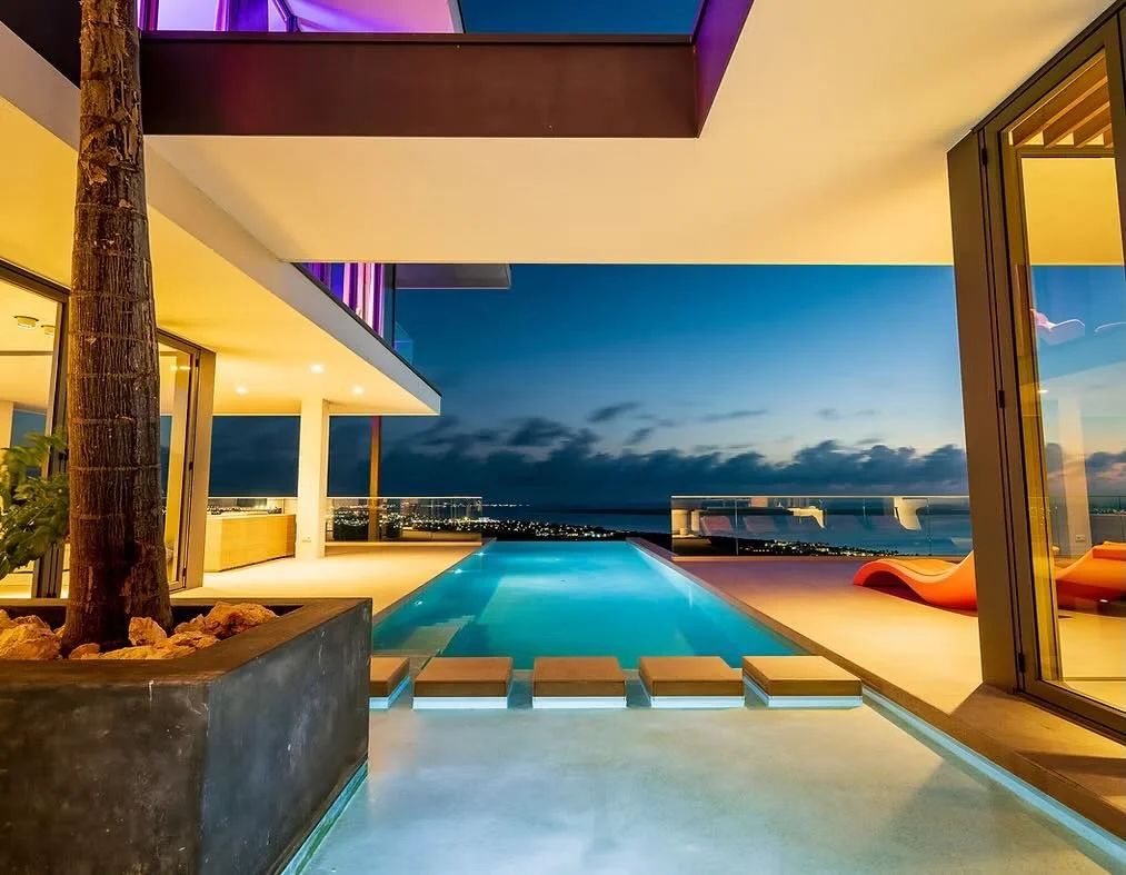 Moderne villa met infinity pool bij zonsondergang, uitzicht op de oceaan, glazen deuren en ligstoelen