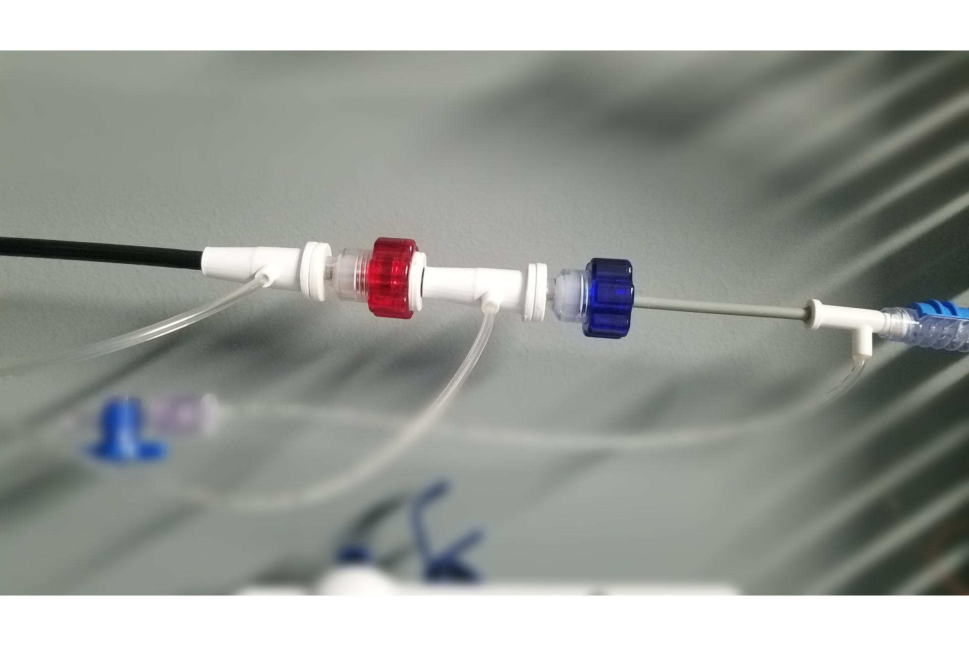 Close-up of medical tubing and connectors with red and blue caps, attached to a wall in a clinical setting.