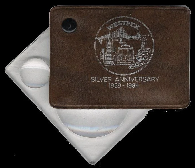 A flip leather case magnifying glass with WESTPEX Silver Anniversary 1959-1984 inscription