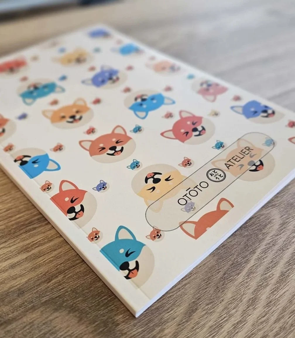 Un carnet de note avec, en couverture, des dessins du shiba de différentes couleurs et expressions, avec le texte "OTOTO ATELIER".