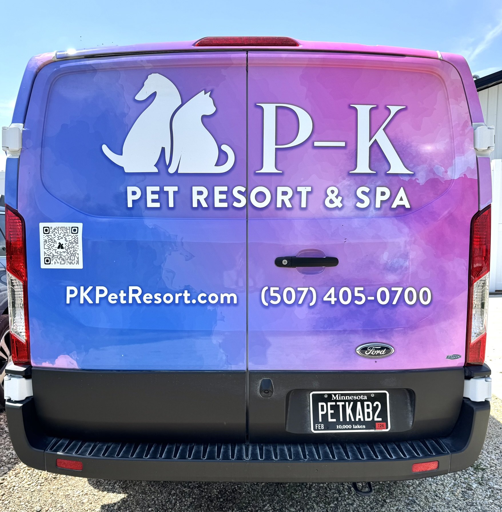 The back of a Ford van with a purple-pink gradient wrap advertising P-K Pet Resort and Spa, featuring a logo with a cat and dog silhouette, website, and phone number.