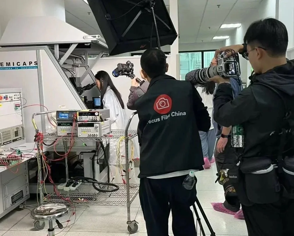 A group of photographers and videographers capturing a woman working with scientific equipment in a laboratory setting.