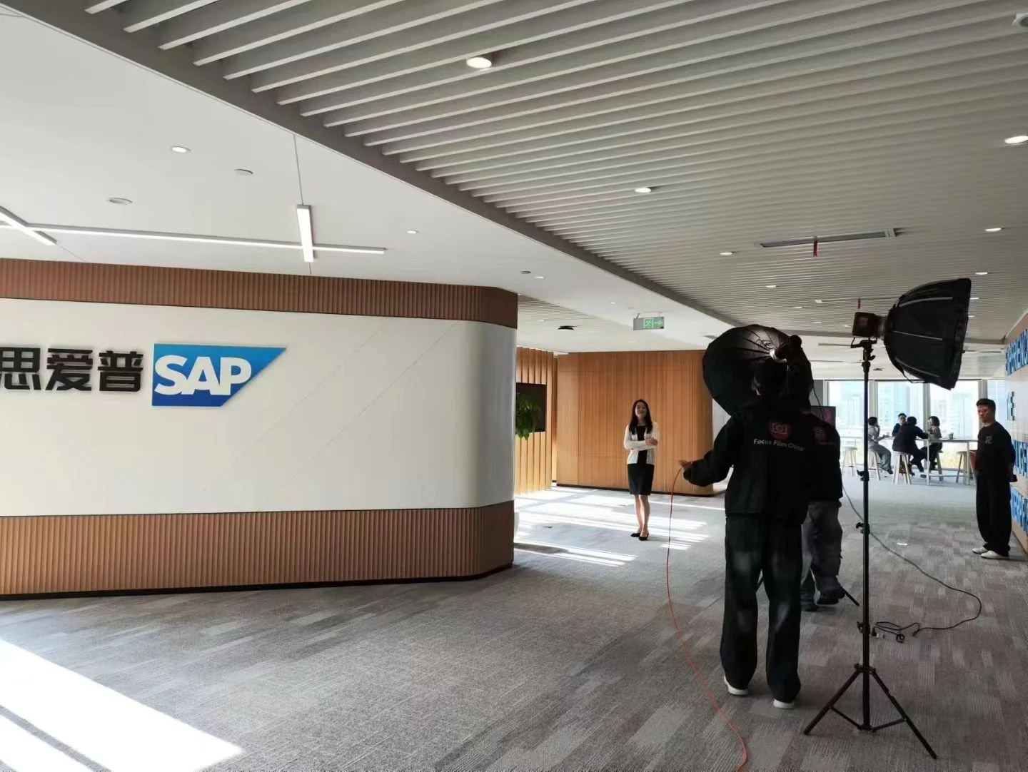 Photographers setting up studio lights for a photoshoot in an office with the SAP logo on the wall, while a woman in business attire stands in the background.