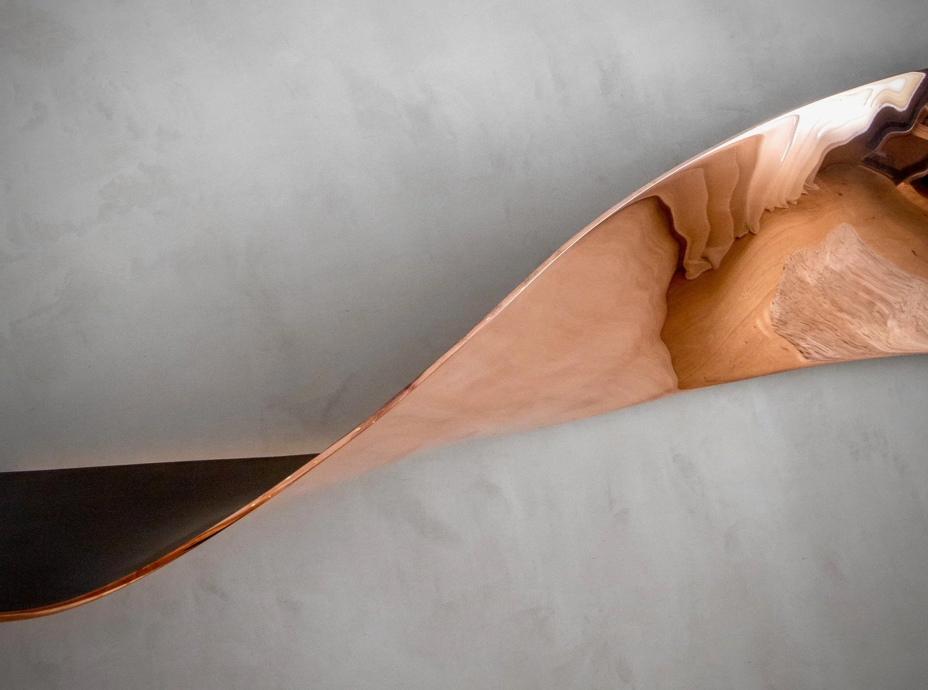 Close-up of a wooden oar with a smooth, polished surface and light wood color, resting against a gray background.