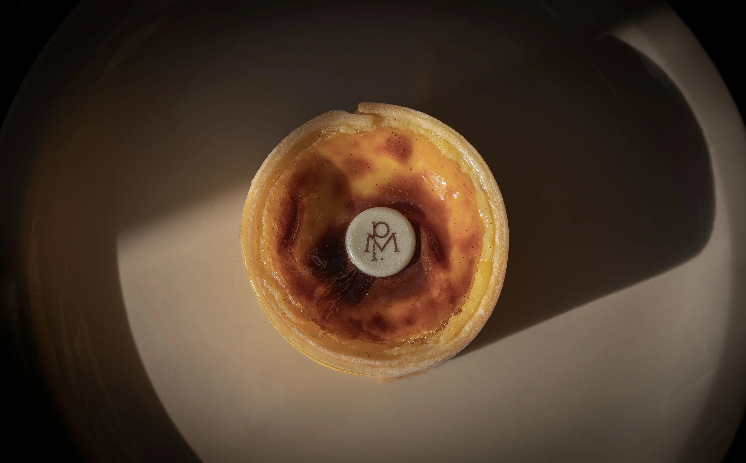 A close-up view of a wine-colored egg tart with a smooth, glossy surface and a logo sticker in the center, against a plain background.