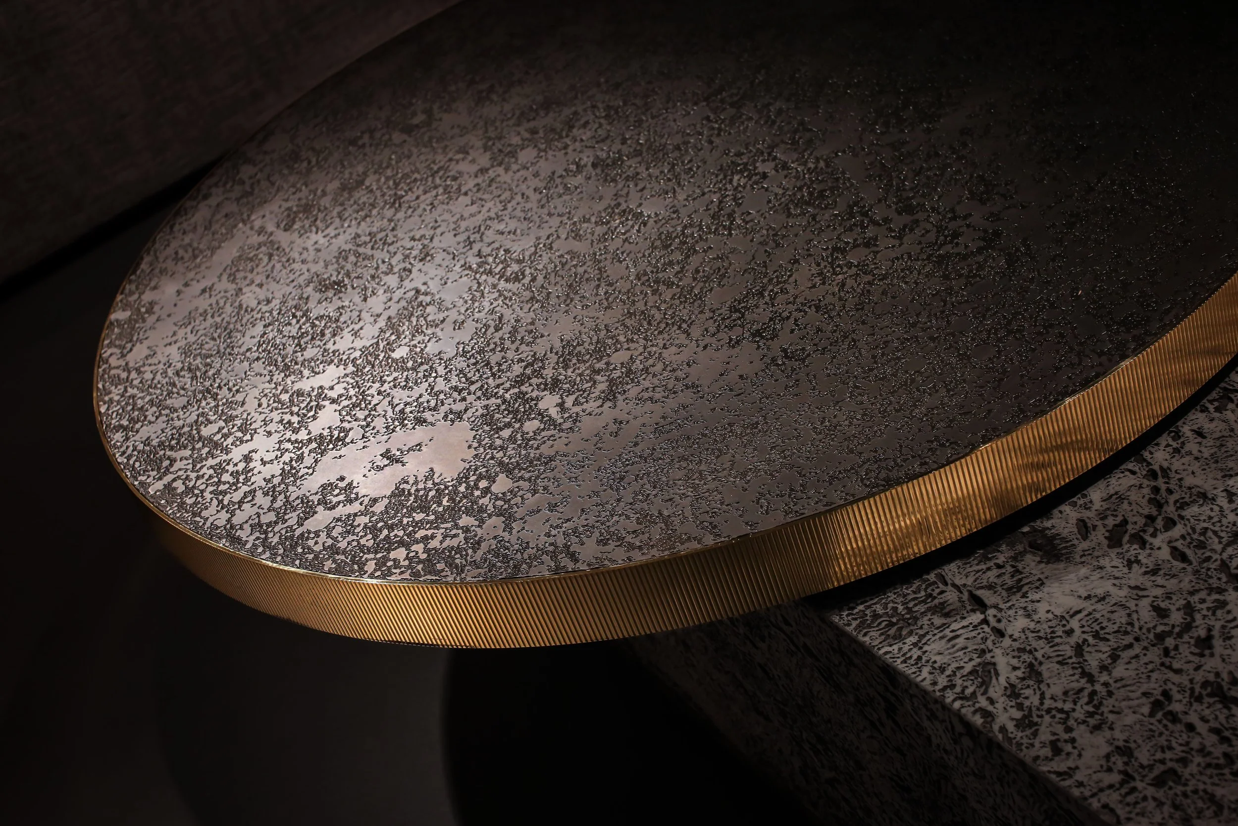 Close-up of a textured, metallic surface with a curved shape, a dark gray speckled pattern, and a gold-colored ribbed edge.