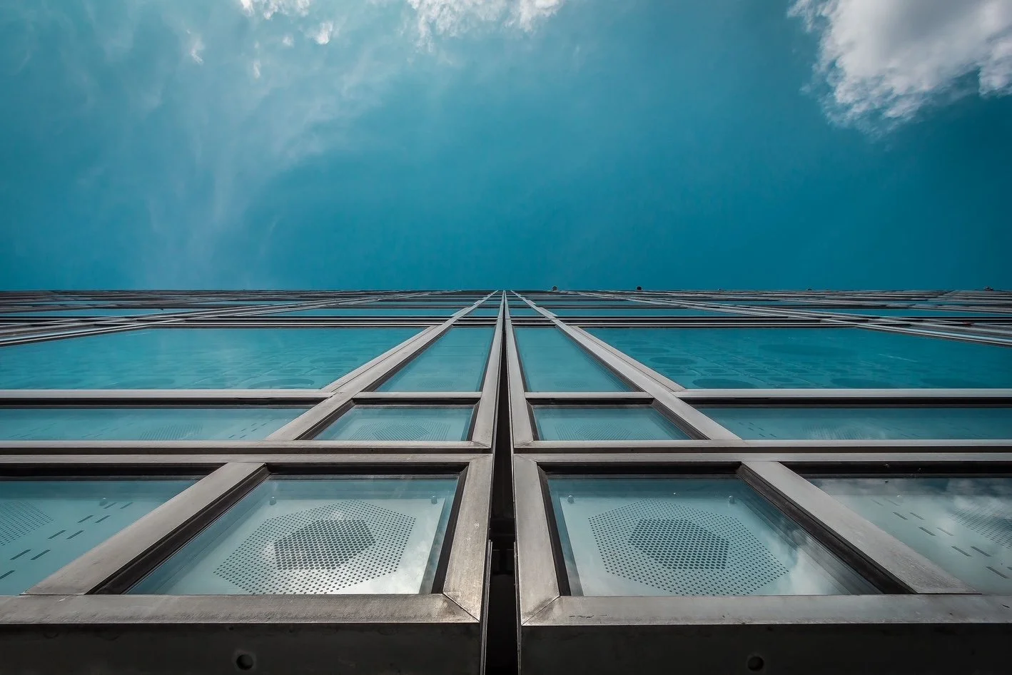 Low-angle view of a modern glass skyscraper reflecting the blue sky and clouds, taken from below.