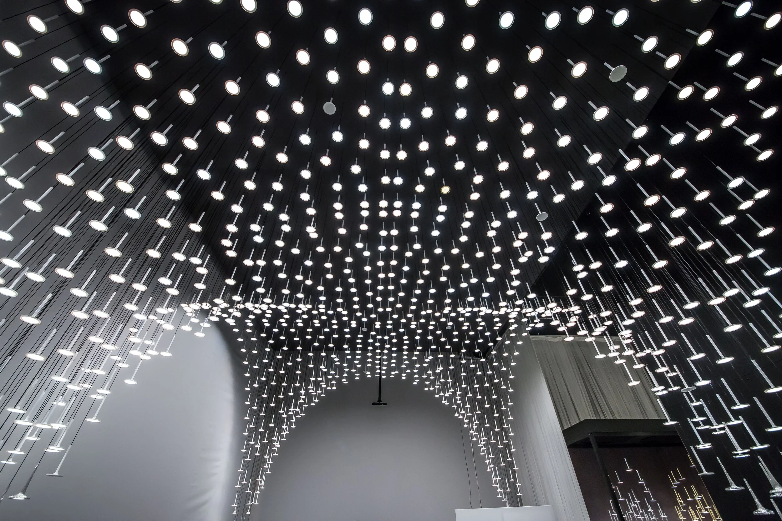 A ceiling installation with many hanging white lights arranged in a curved pattern.