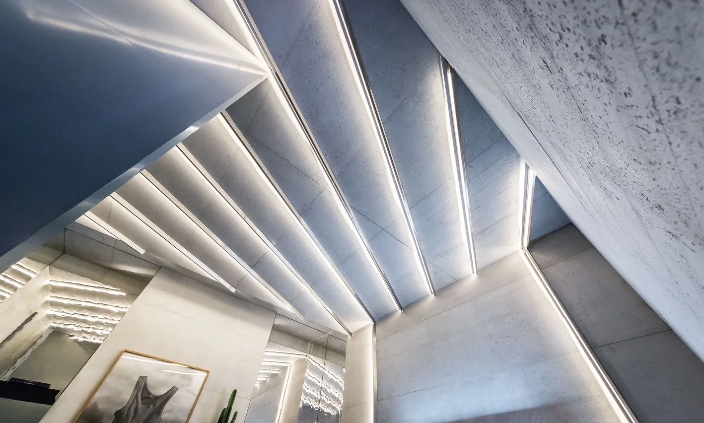 Modern interior with a staircase, illuminated with sleek linear LED lighting on the ceiling and walls, featuring minimal decor and a framed picture.