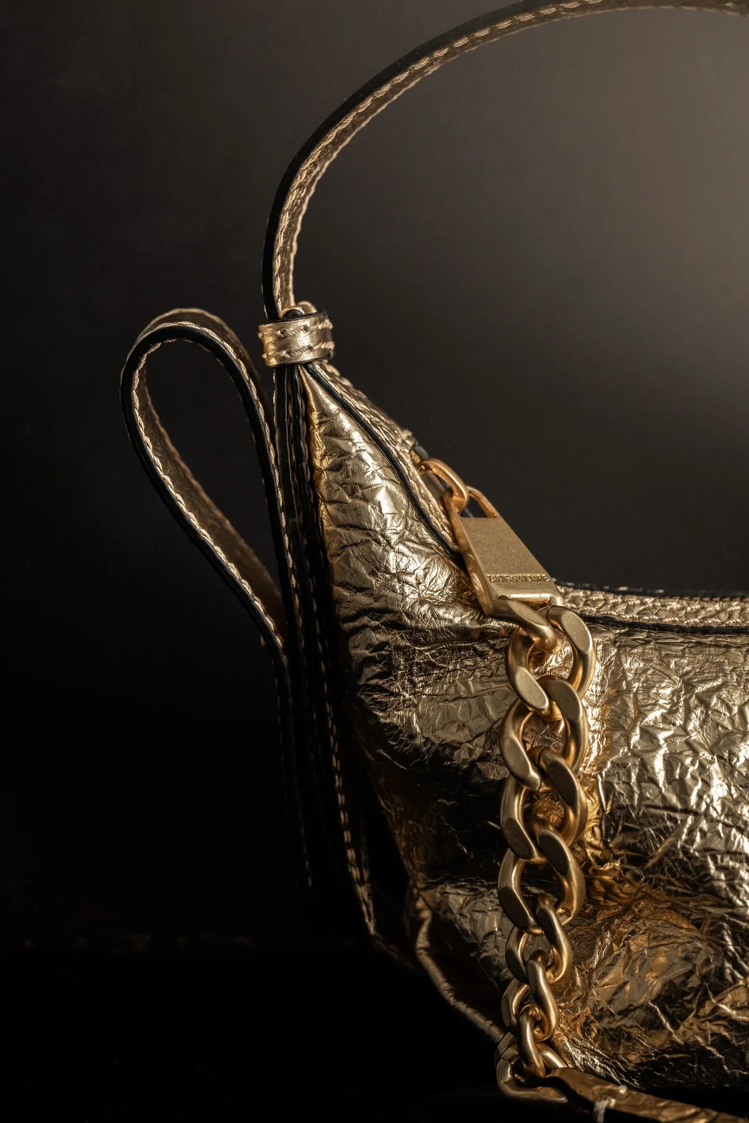 A metallic silver handbag with a gold chain strap, set against a dark background.