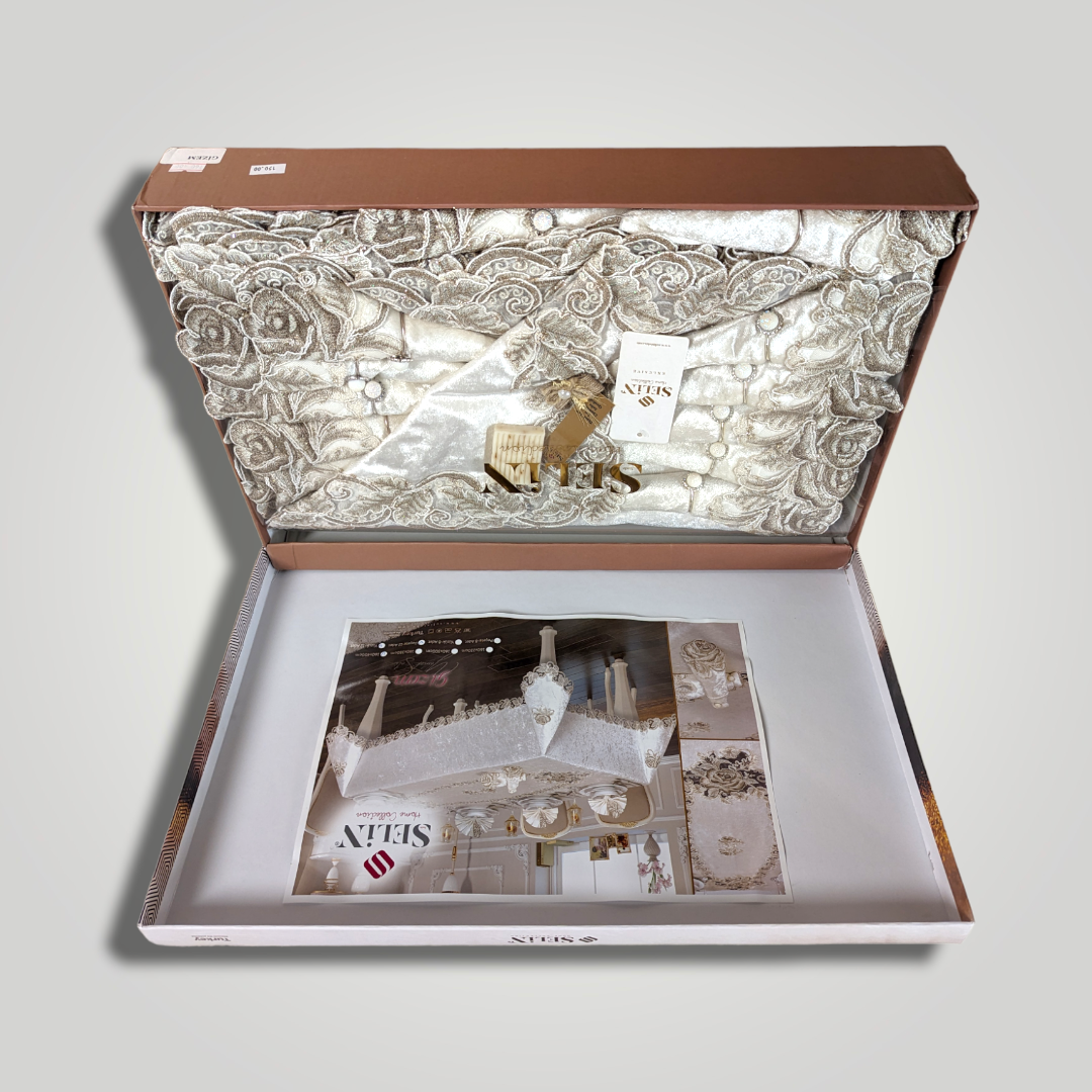 Open jewelry box containing a silver fabric interior with intricate floral embroidery, and a printed magazine page with jewelry images underneath.