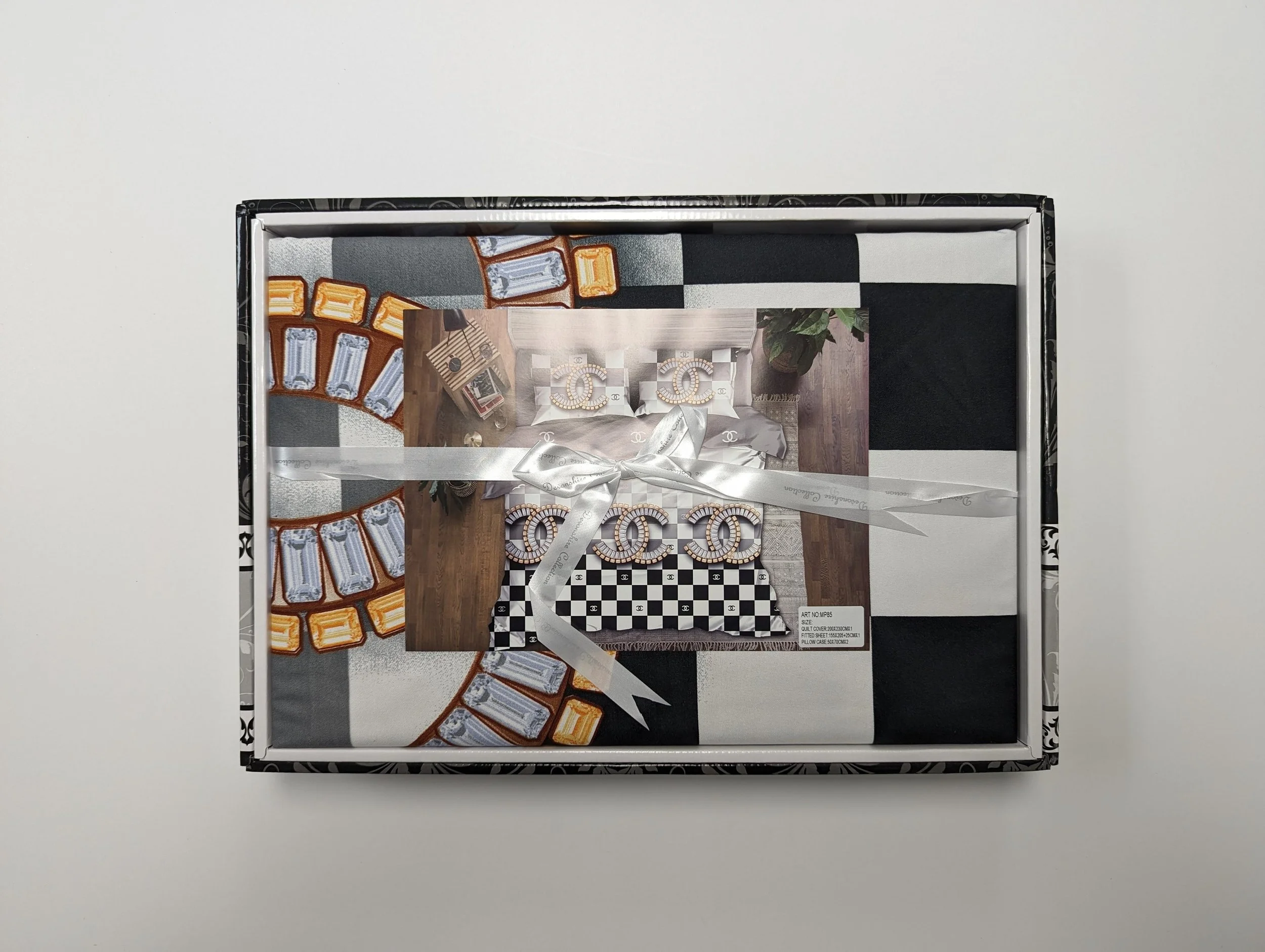 Gift box decorated with a photo, ribbon, and designer packaging, containing multiple frames with a street scene, a checkerboard, and furniture, all themed around Chanel luxury branding.