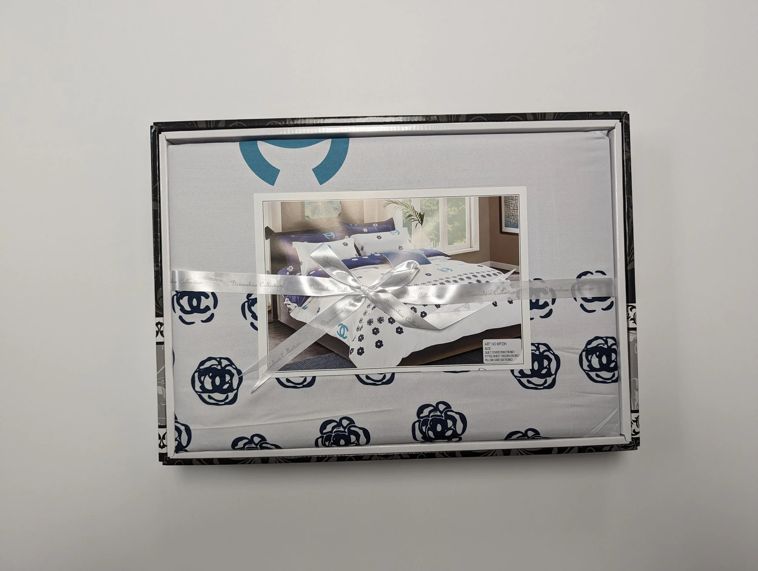 Packaging box for a bedding set with a picture of a bedroom on the front, decorated with blue and white linens, topped with a white ribbon.