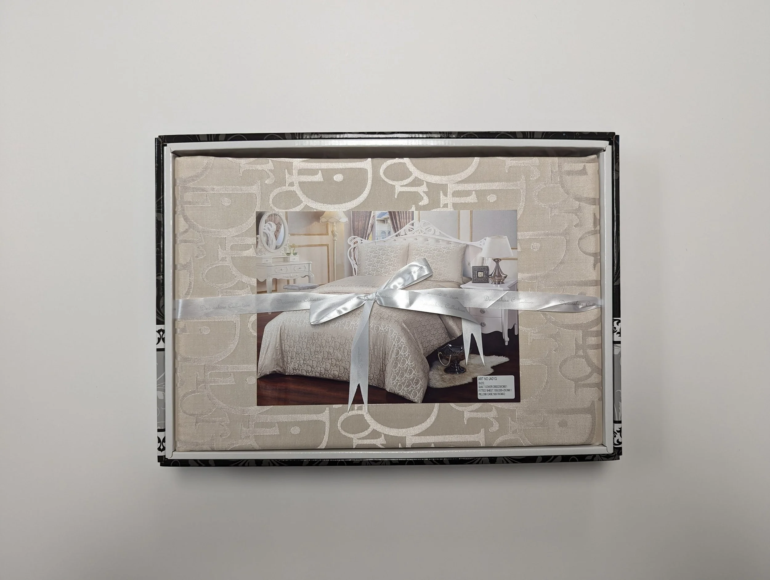 A bedroom set, including a bed with a headboard, bedside tables, and lamps, is displayed in packaging with a white ribbon.