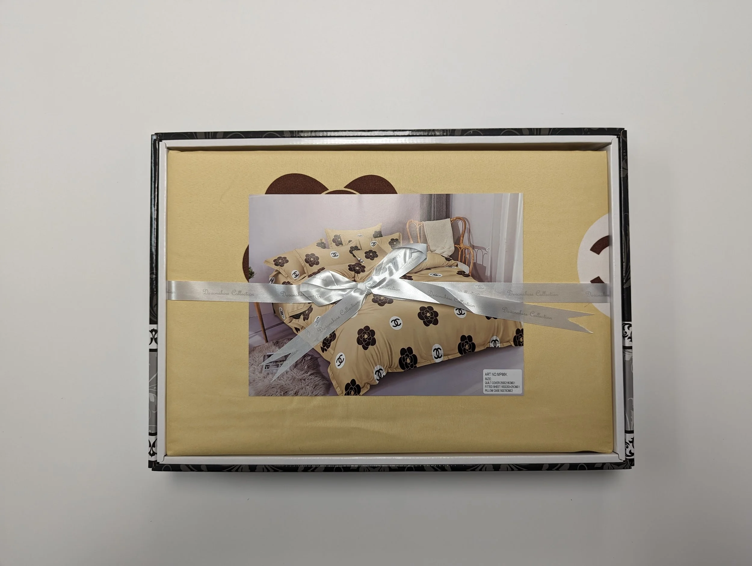 A boxed set of bedding featuring a floral pattern with Chanel logos, wrapped with a white ribbon.