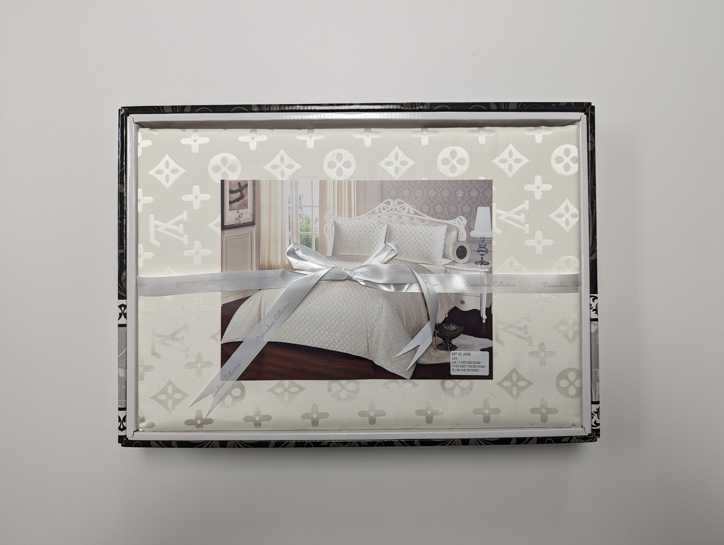 Box of white bedding with a picture of a bedroom on the front, wrapped with a white ribbon.