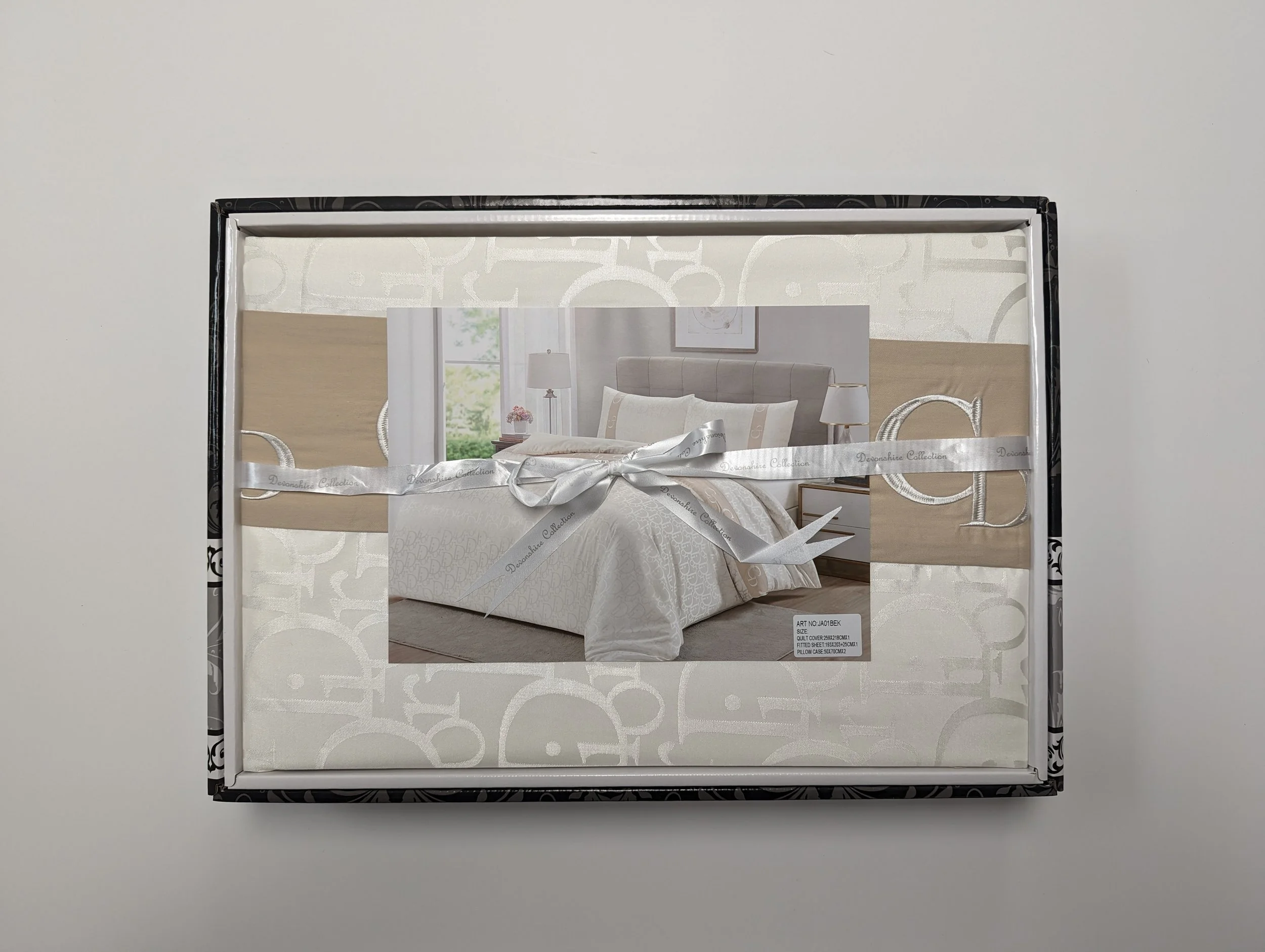 A boxed set of white bedding with a bed, pillows, and bedside tables, shown in an image on the packaging.