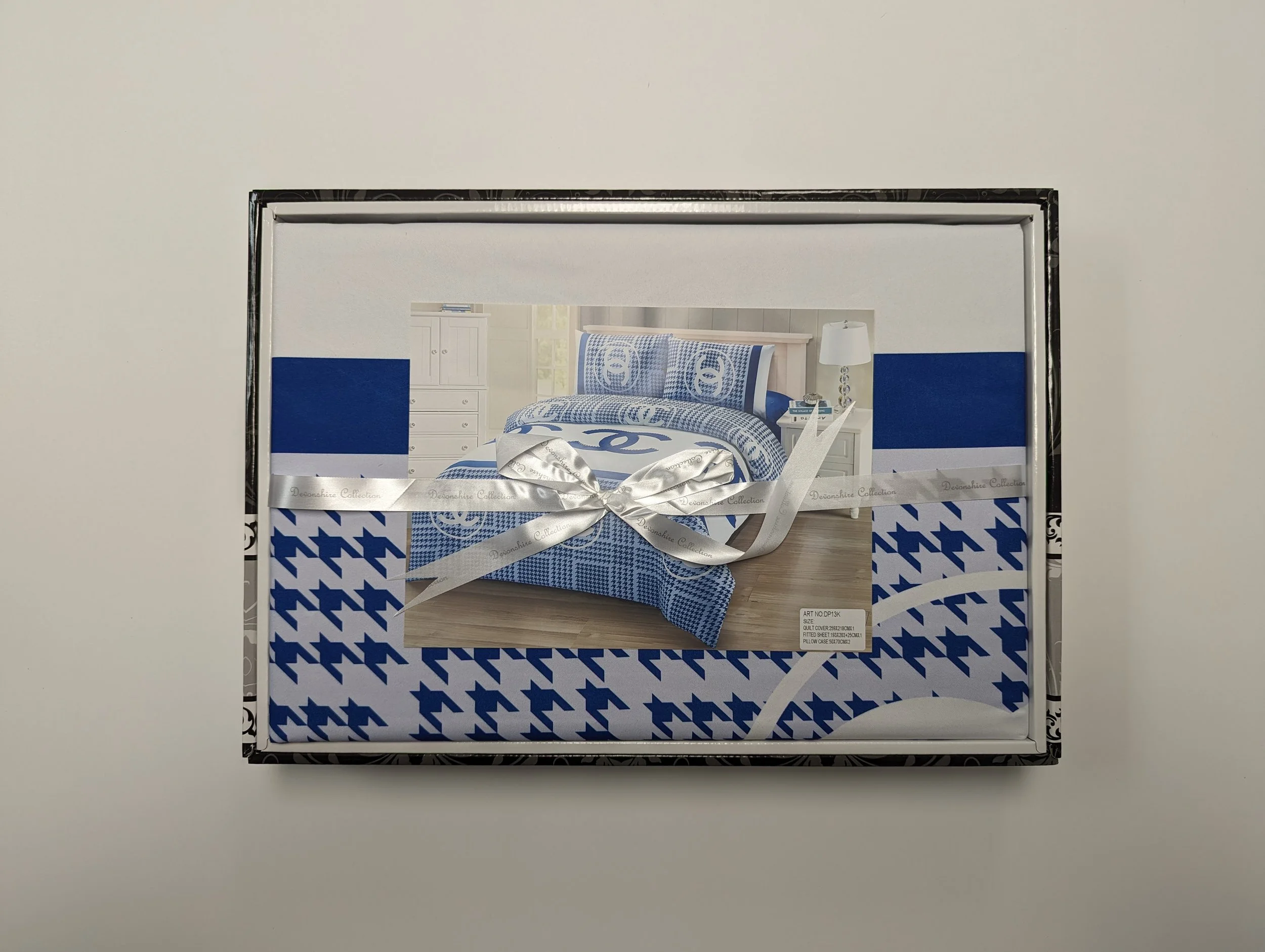Boxed bed set with blue and white houndstooth and circular patterned bedding, wrapped with a silver ribbon.