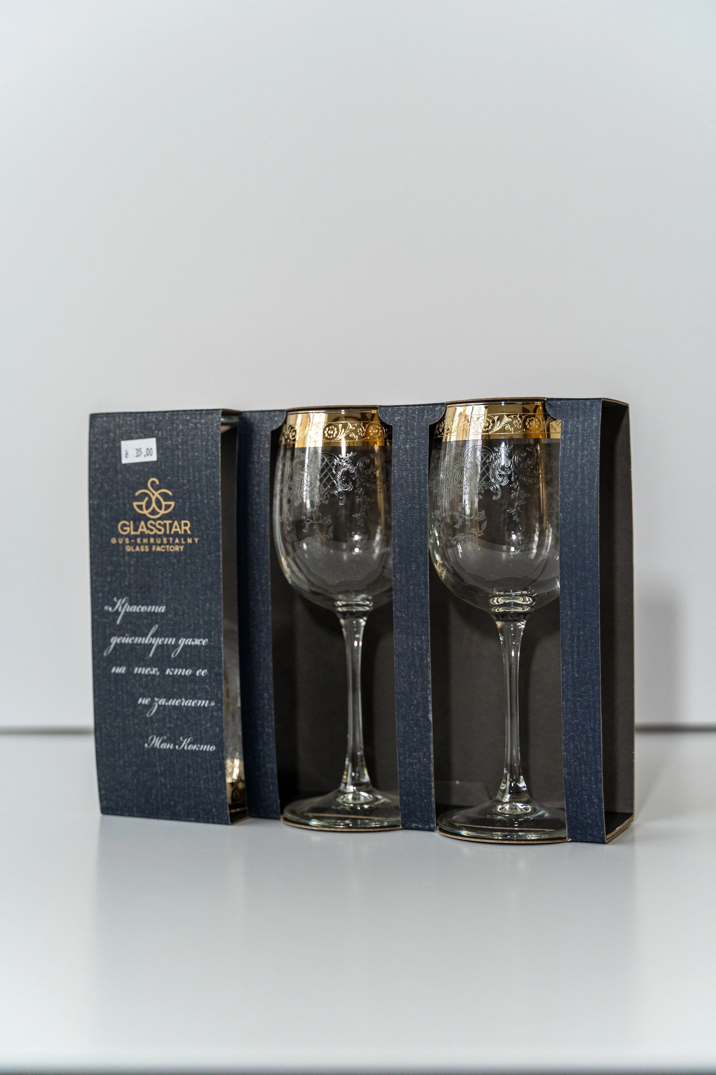Two decorated wine glasses with gold rims in a blue and black packaging box on a white surface.