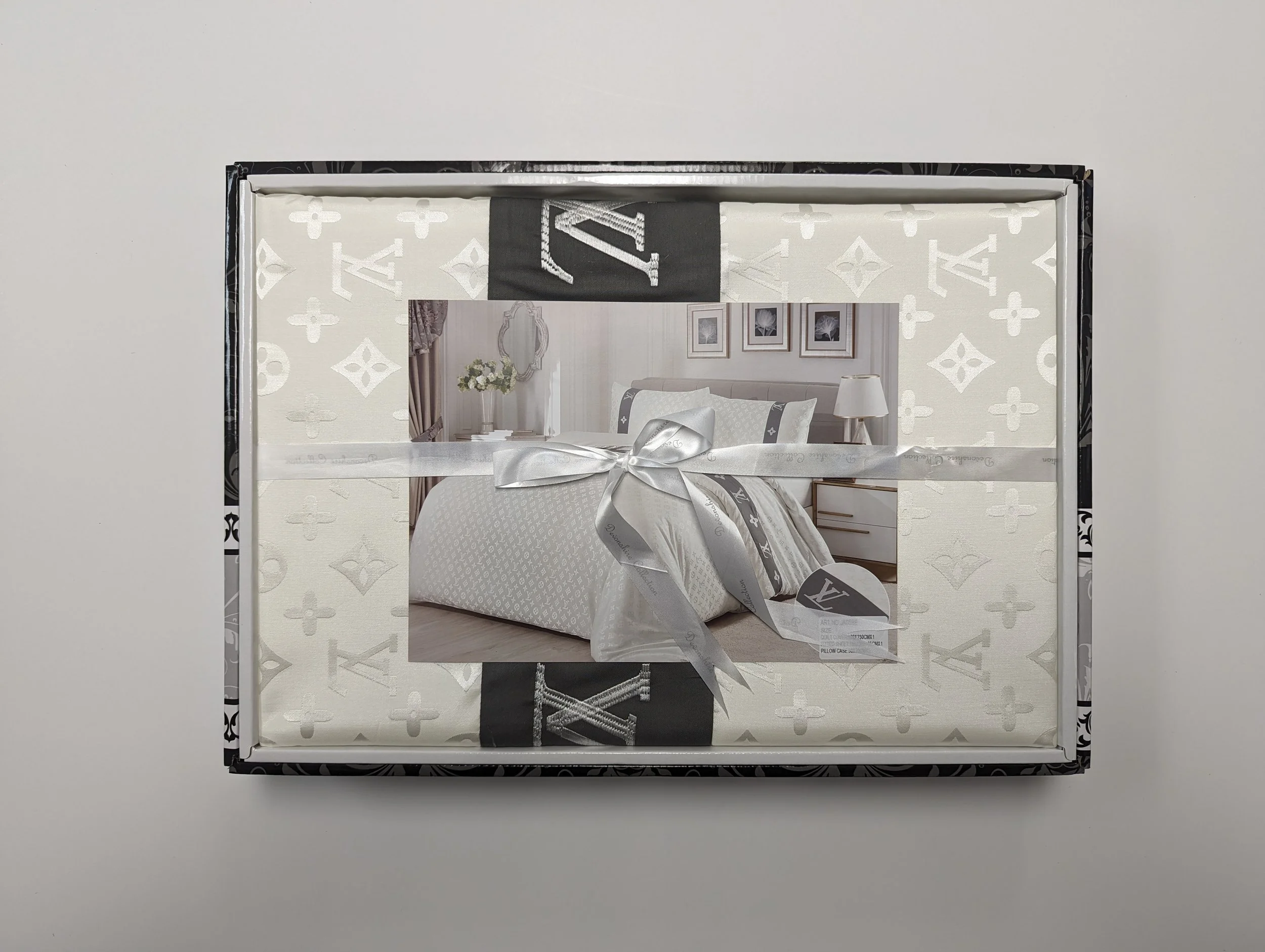 A wrapped gift box featuring a Louis Vuitton pattern, tied with a silver ribbon, and a photograph of a bedroom scene on top.
