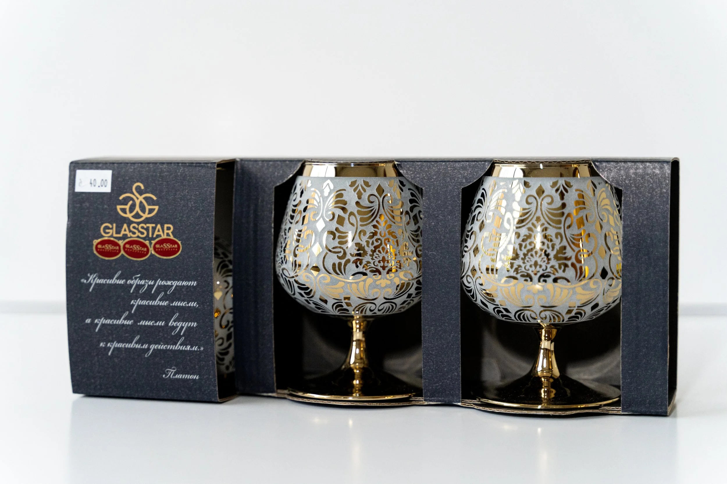 A set of two decorative glass cups with gold and silver floral patterns in a black display box.
