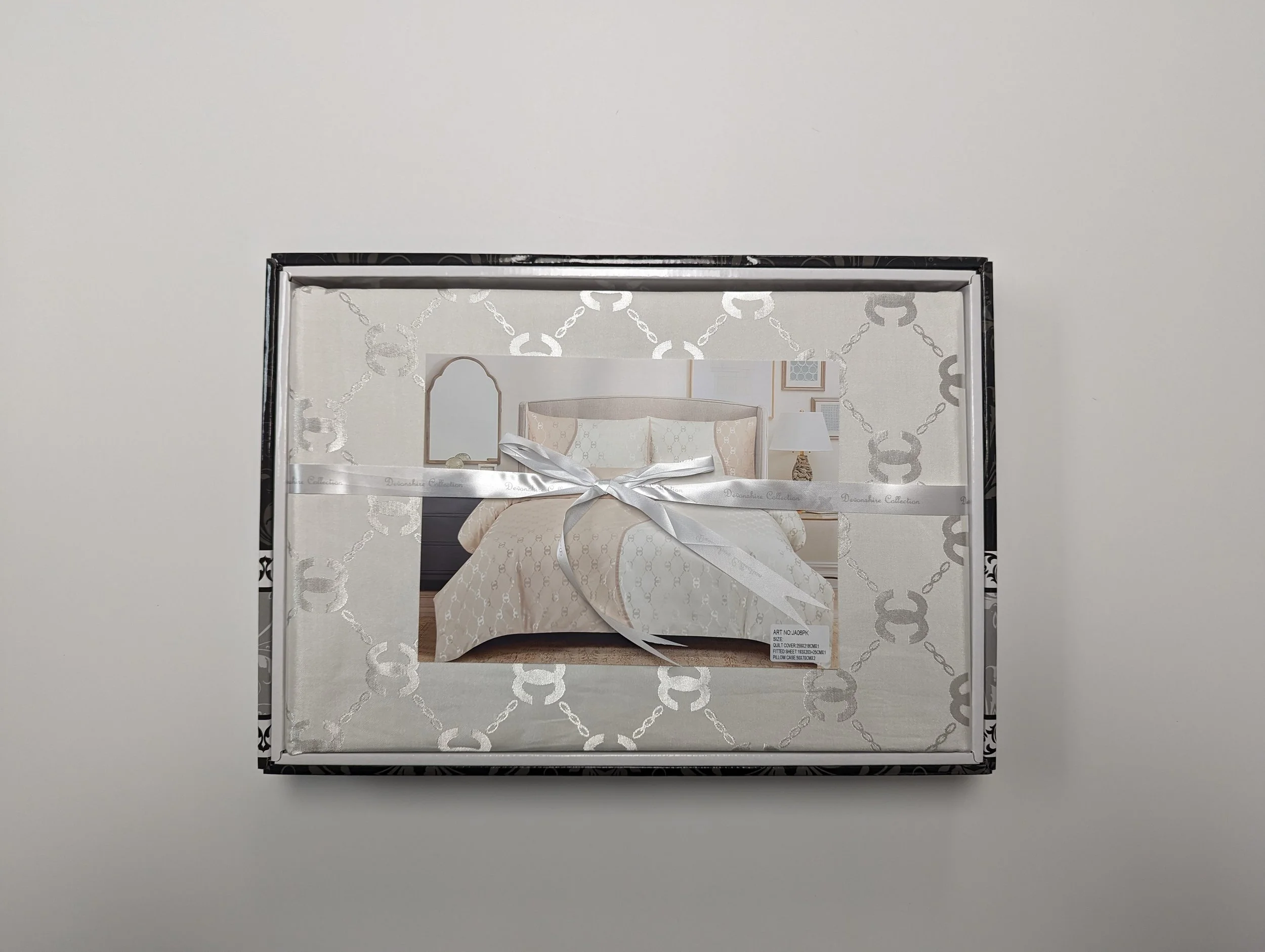 Box of bedding or linens with a bedroom scene on the front, tied with a silver ribbon, set on a plain, white surface.