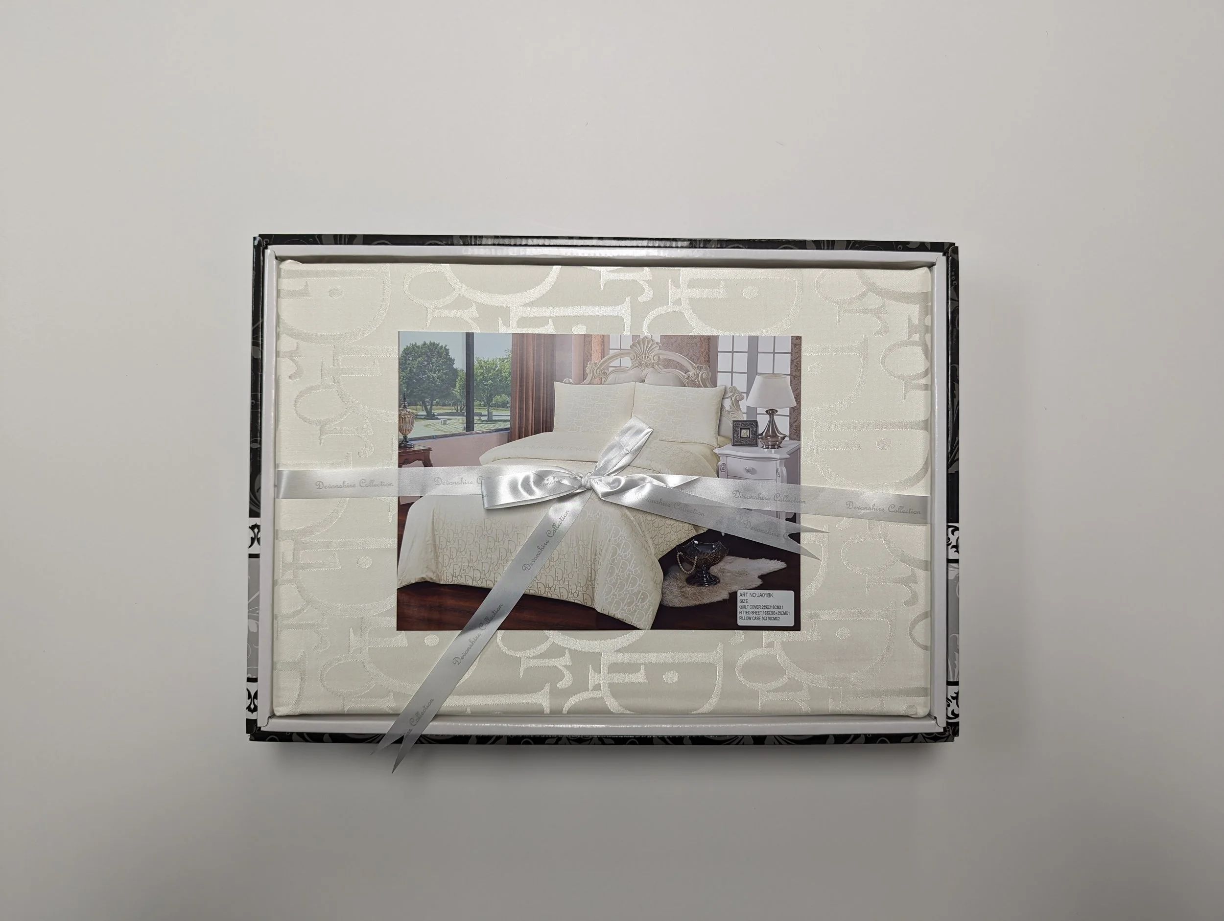 A boxed set of white sheet and pillowcases with a photo of a bedroom on the front, tied with a silver ribbon.