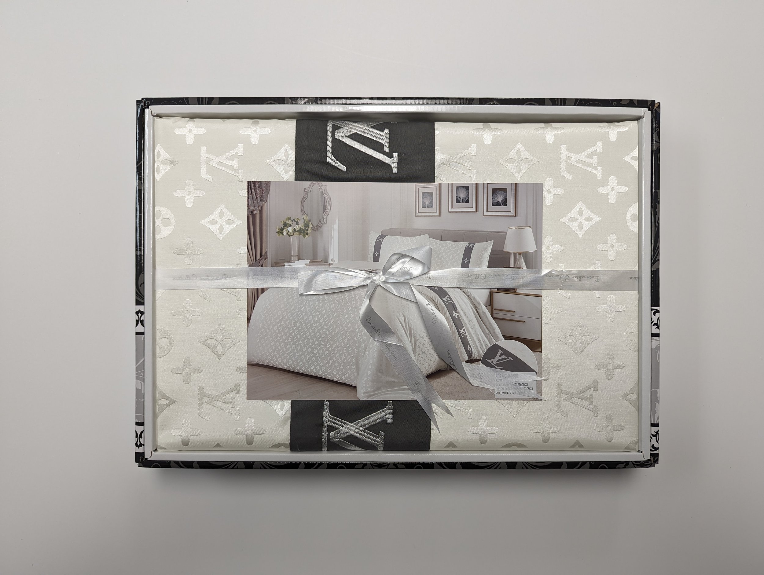 A boxed set of luxury bedding with a photograph of a bedroom on the packaging, wrapped with a silver ribbon.