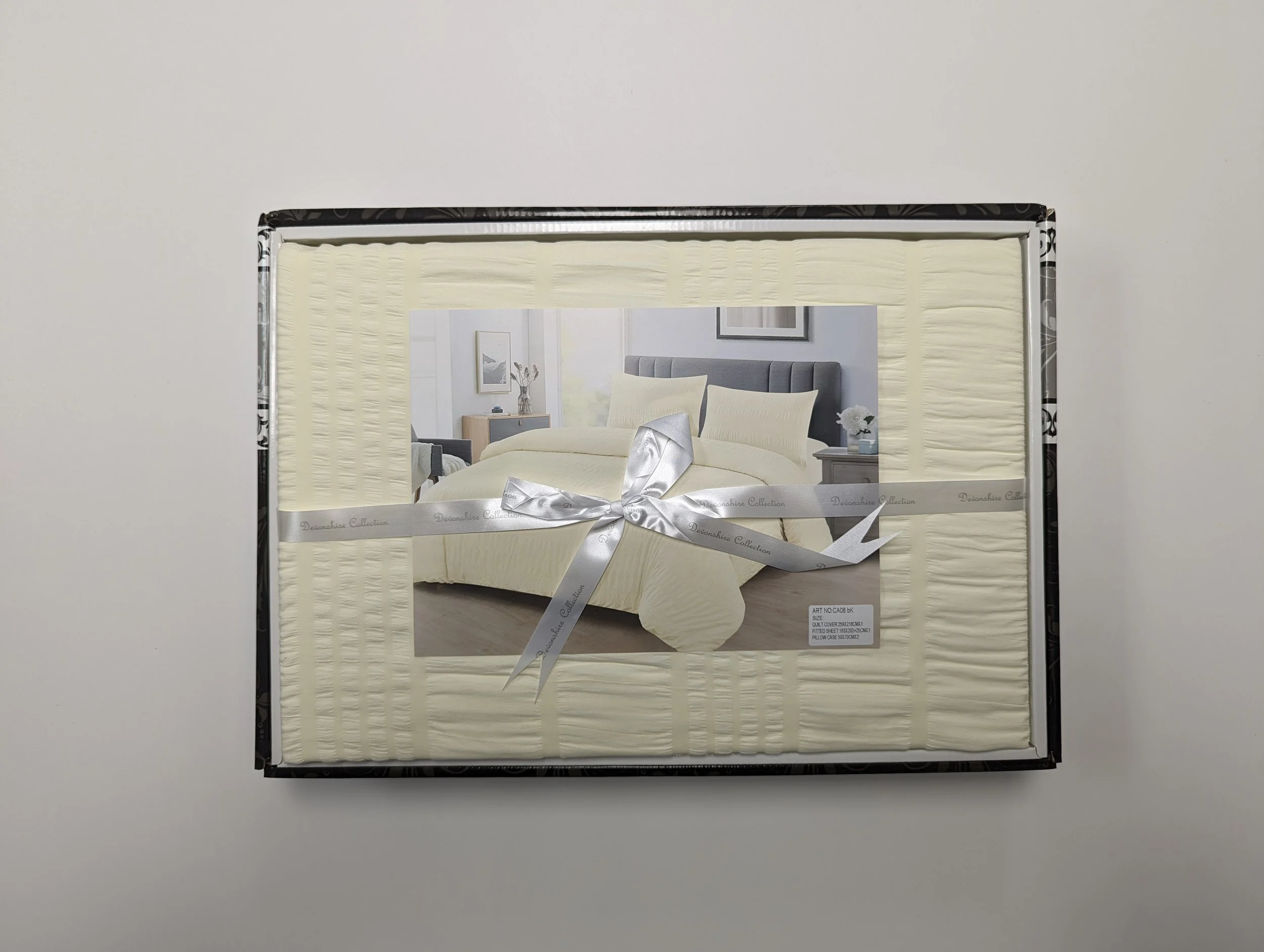 Packaging for a cream-colored bedding set featuring a picture of a bedroom with a bed, pillows, and side tables with decor.