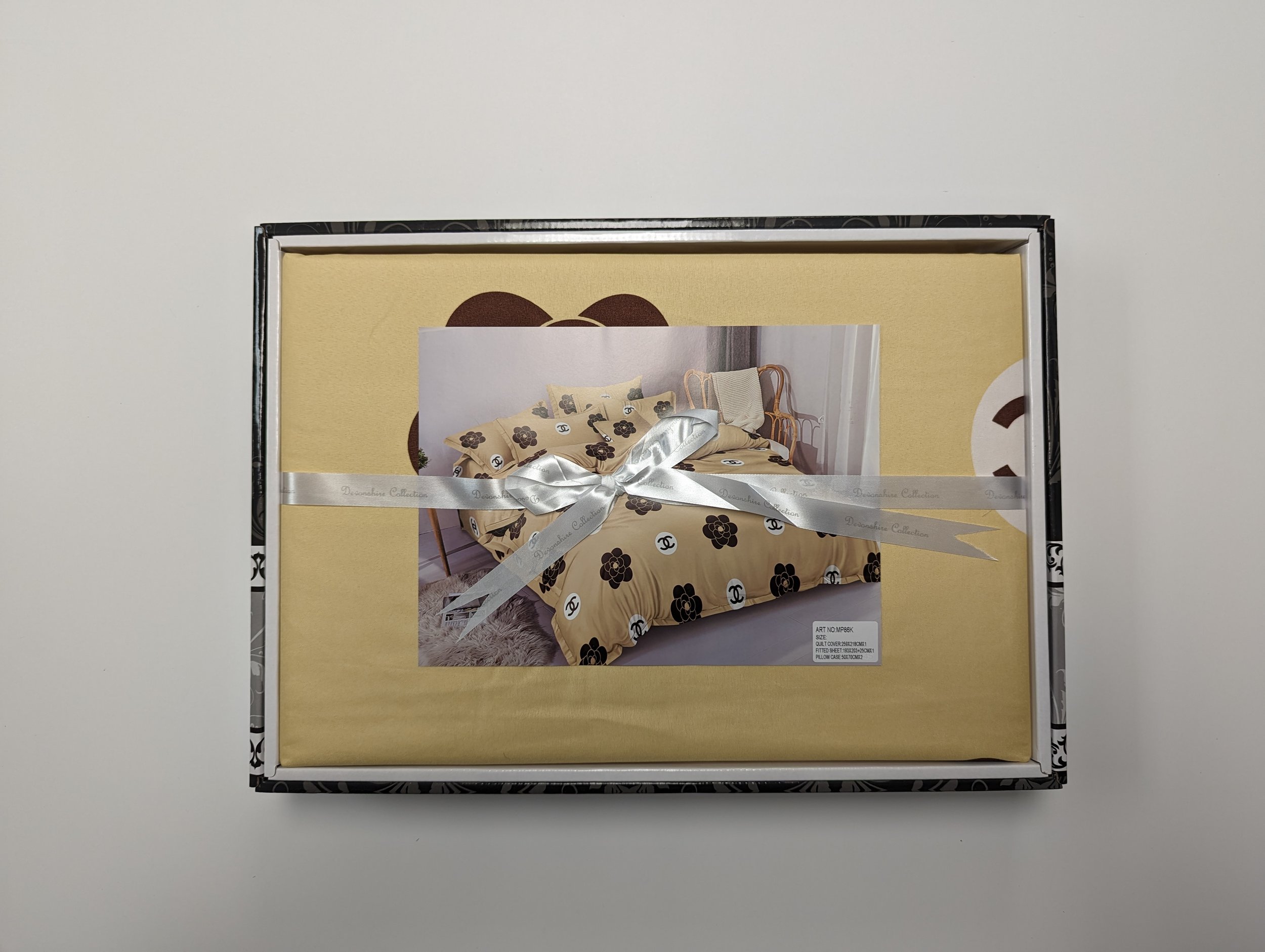 A packaged duvet cover set with a picture of a bed with beige and black floral patterned bedding, tied with a silver ribbon.