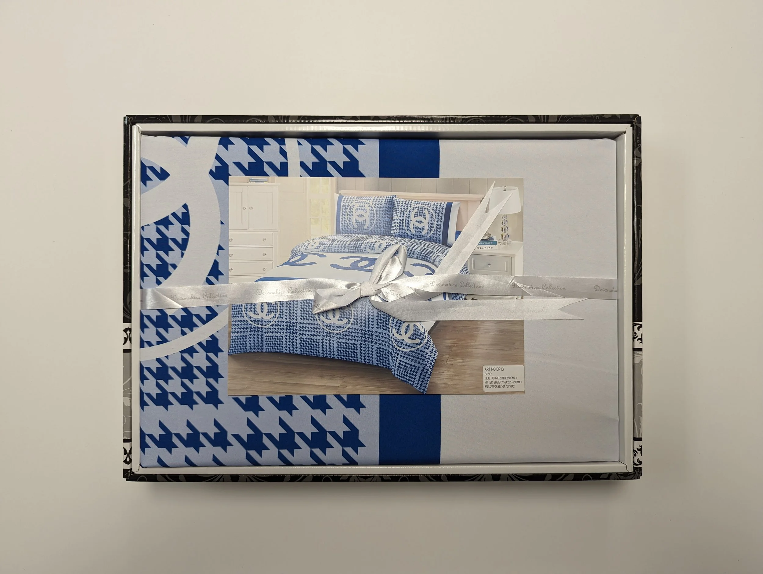 Box containing a blue and white bed set with houndstooth and geometric patterns, wrapped with a white ribbon