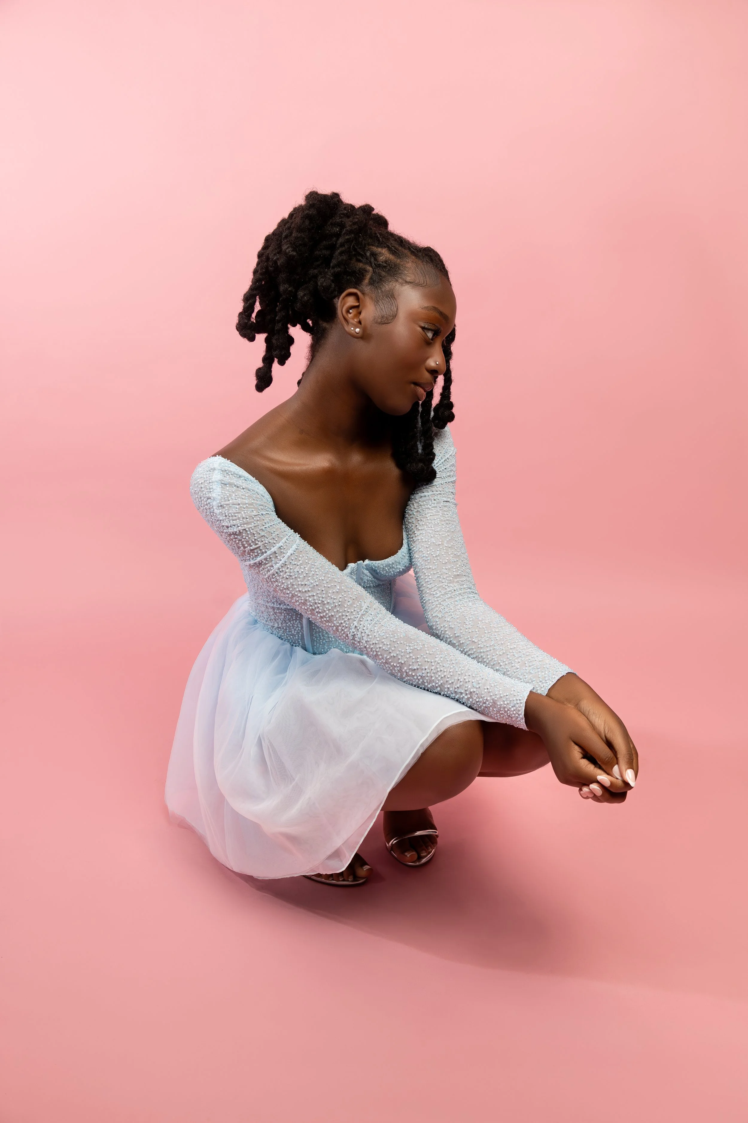 Person in light blue dress crouching against pink background