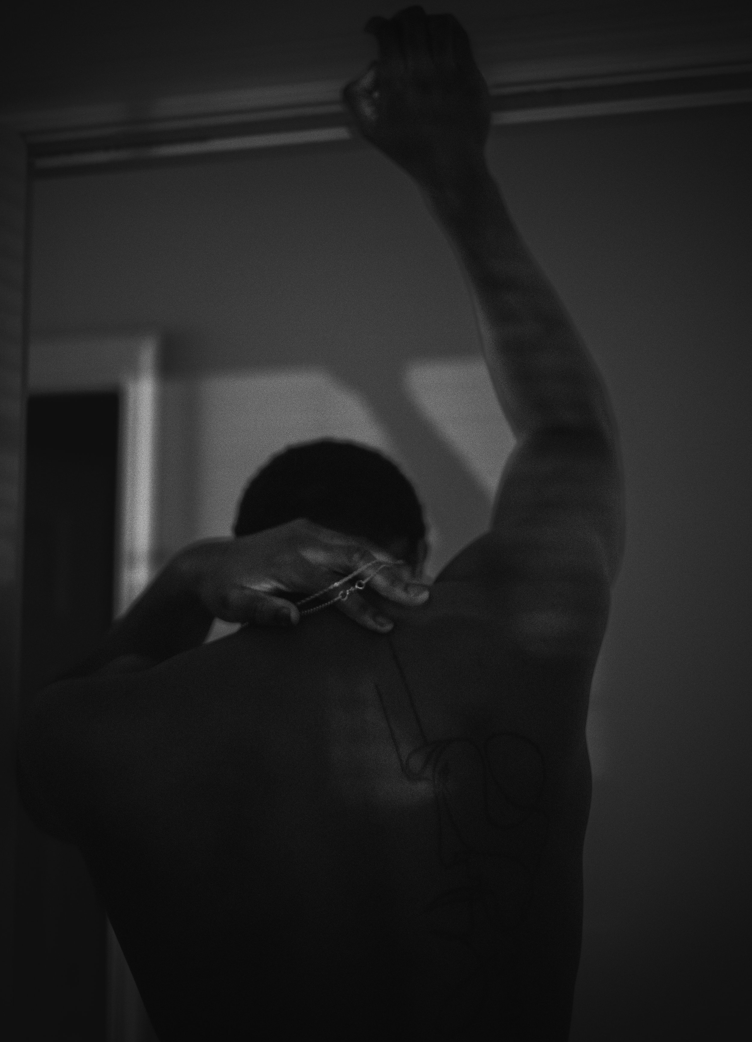 Back view of a person with a line drawing tattoo on their back, one arm raised, holding necklace.