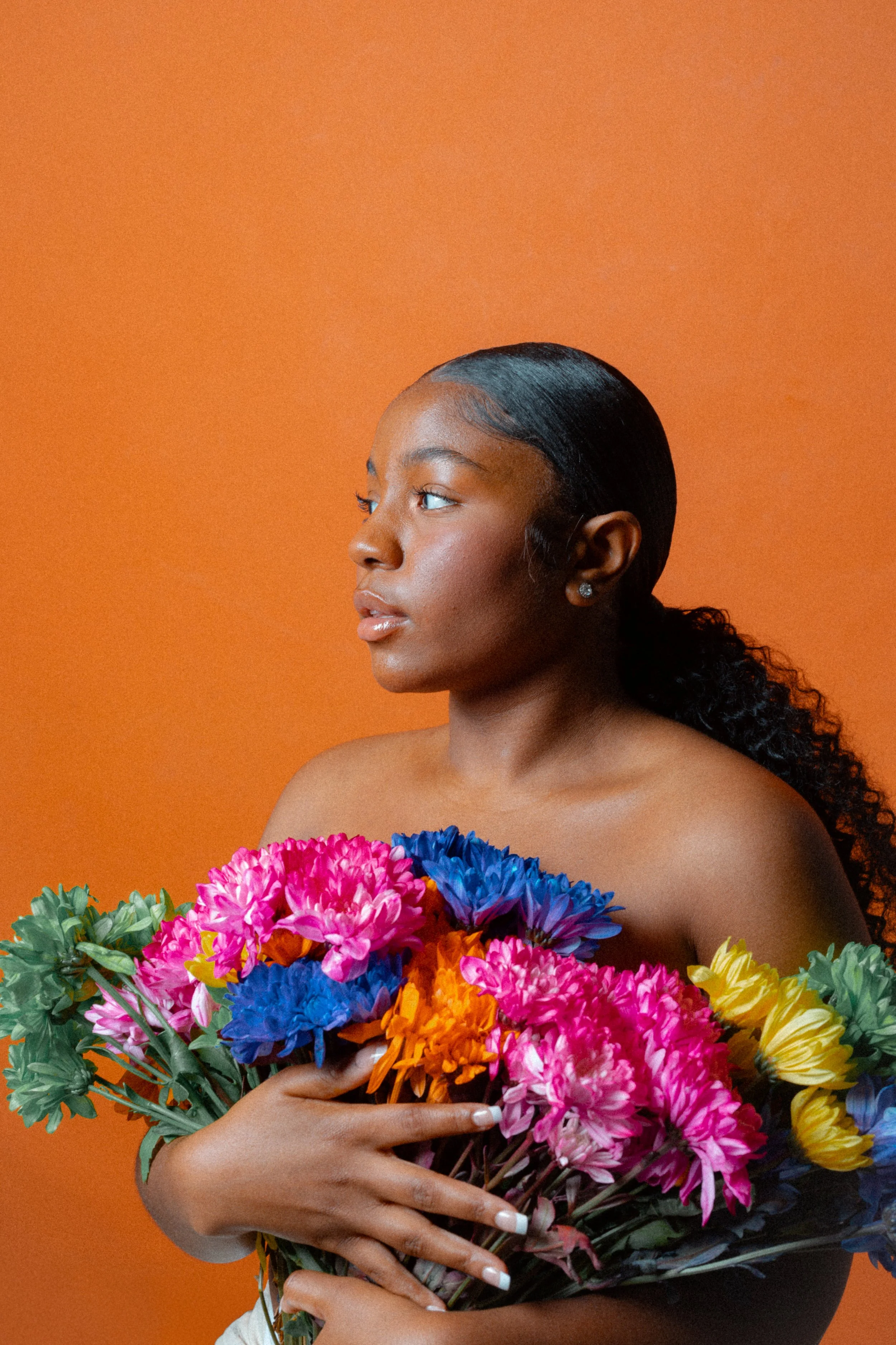 Woman holding colorful flowers against an orange background.