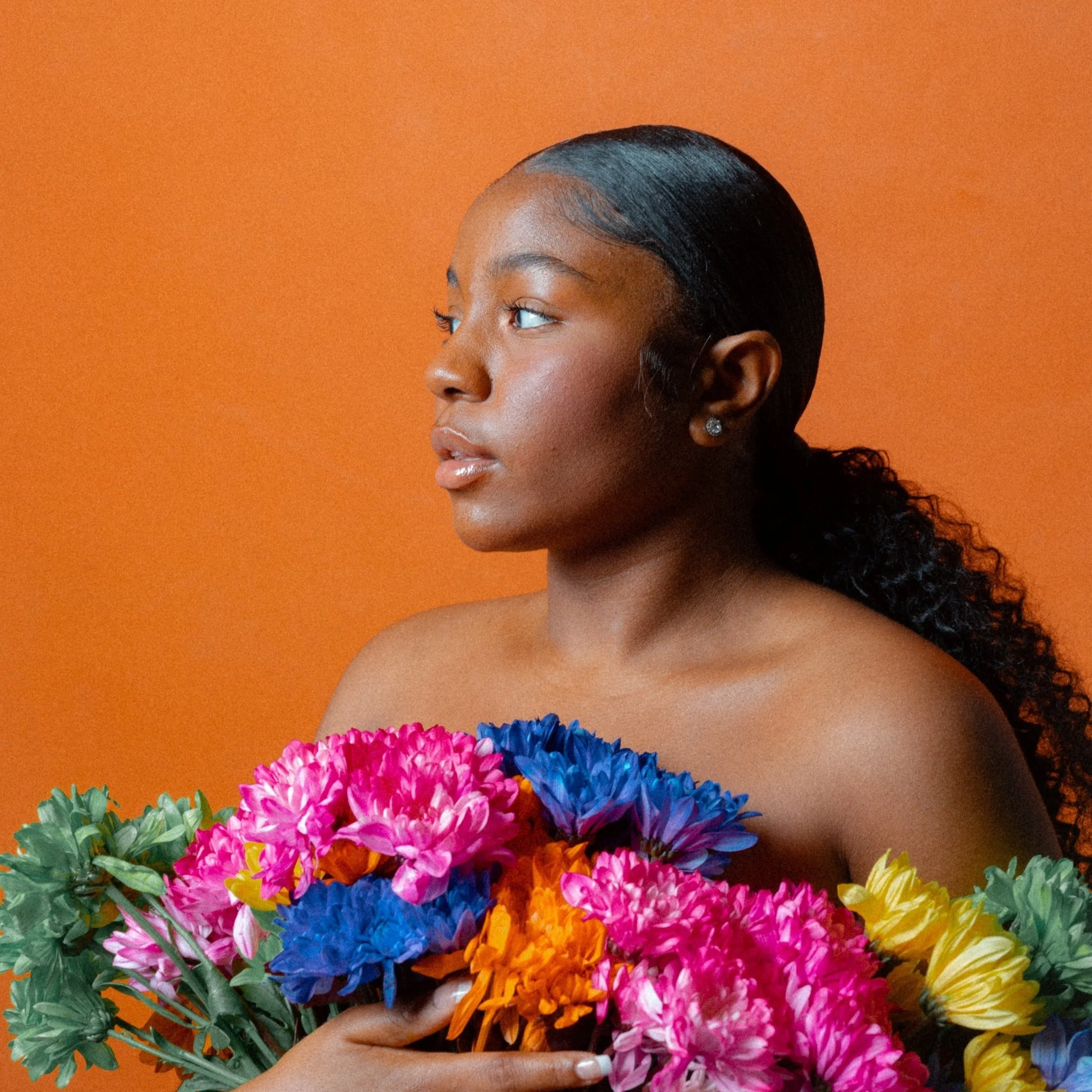 A person holding a colorful bouquet of flowers against an orange background.