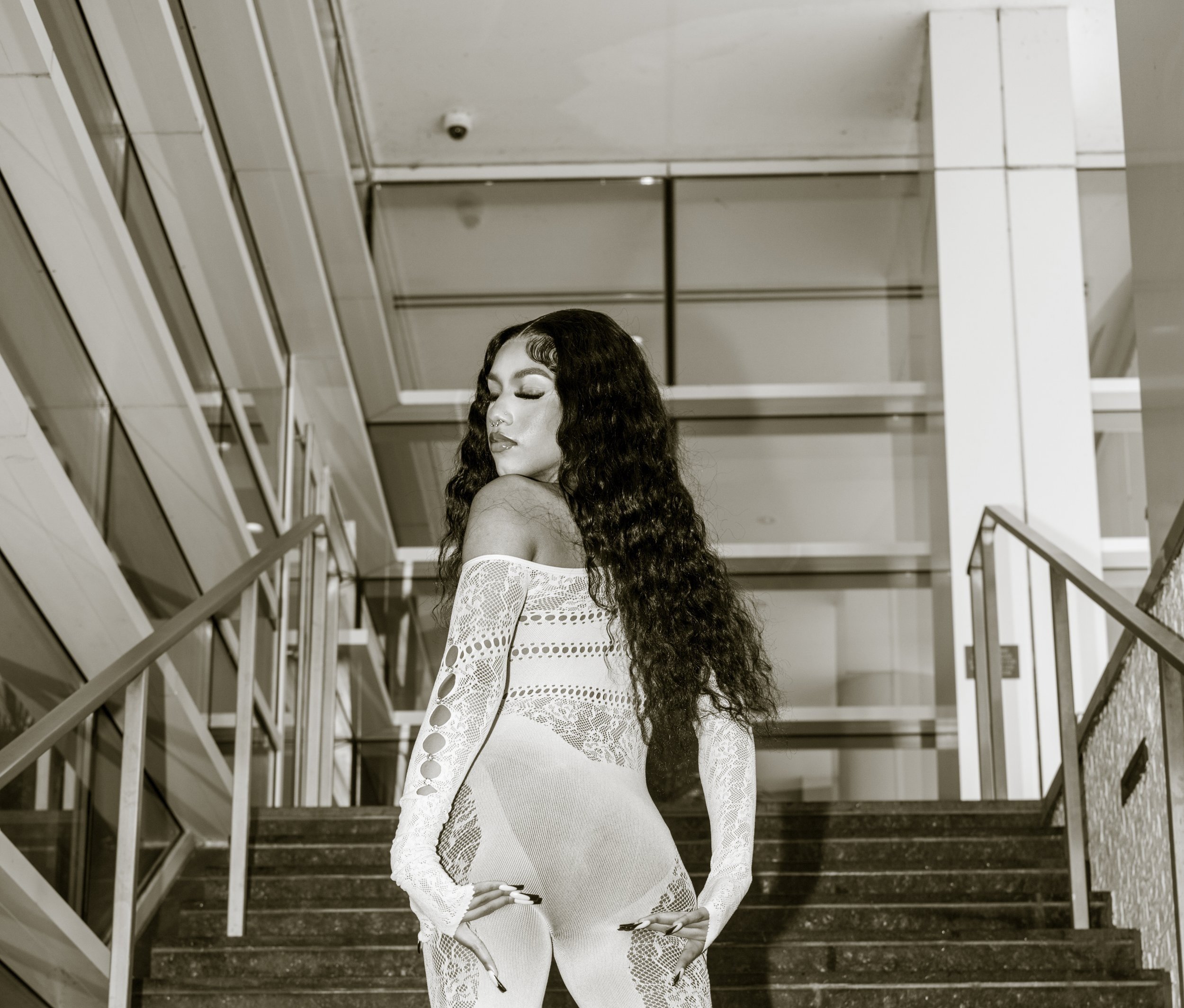 Woman in lace outfit posing on a stairway indoors.