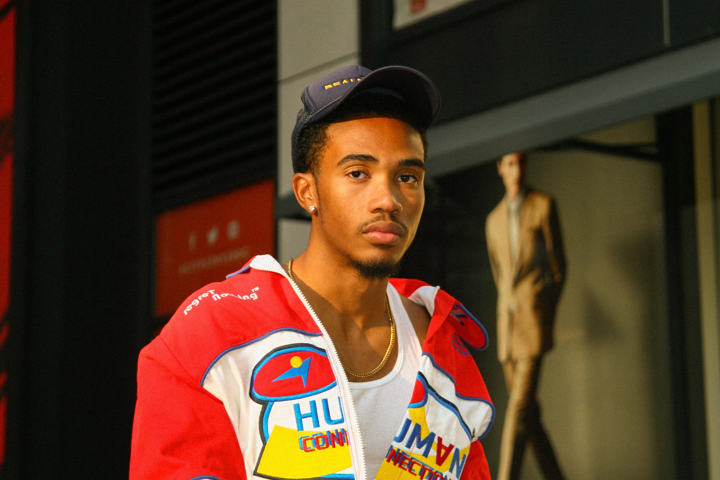 A man in a colorful jacket and baseball cap standing outdoors, looking at the camera. The jacket has "Human Connection" text on it.