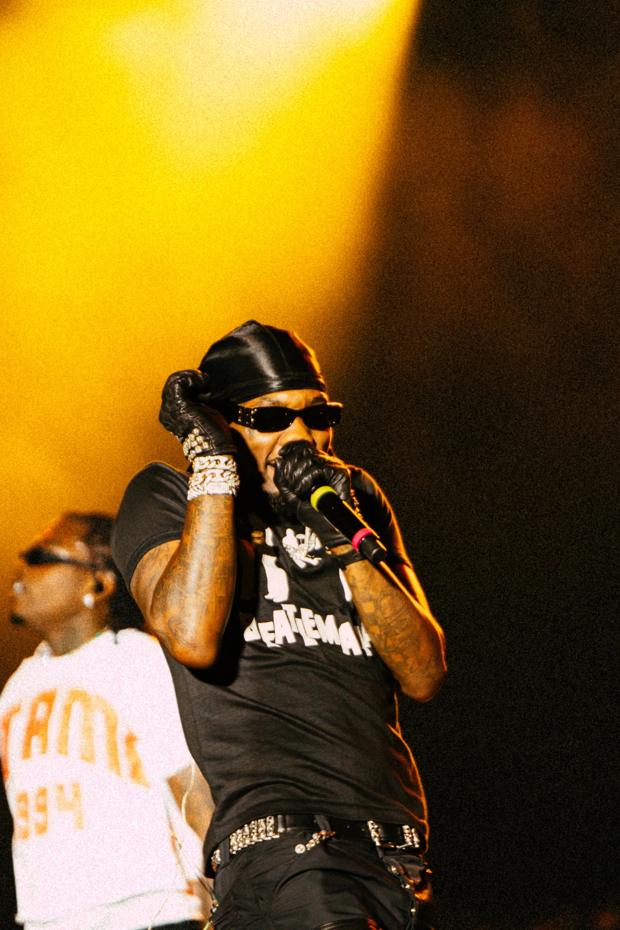 Musician performing on stage with microphone, wearing sunglasses and gloves, warm yellow lighting