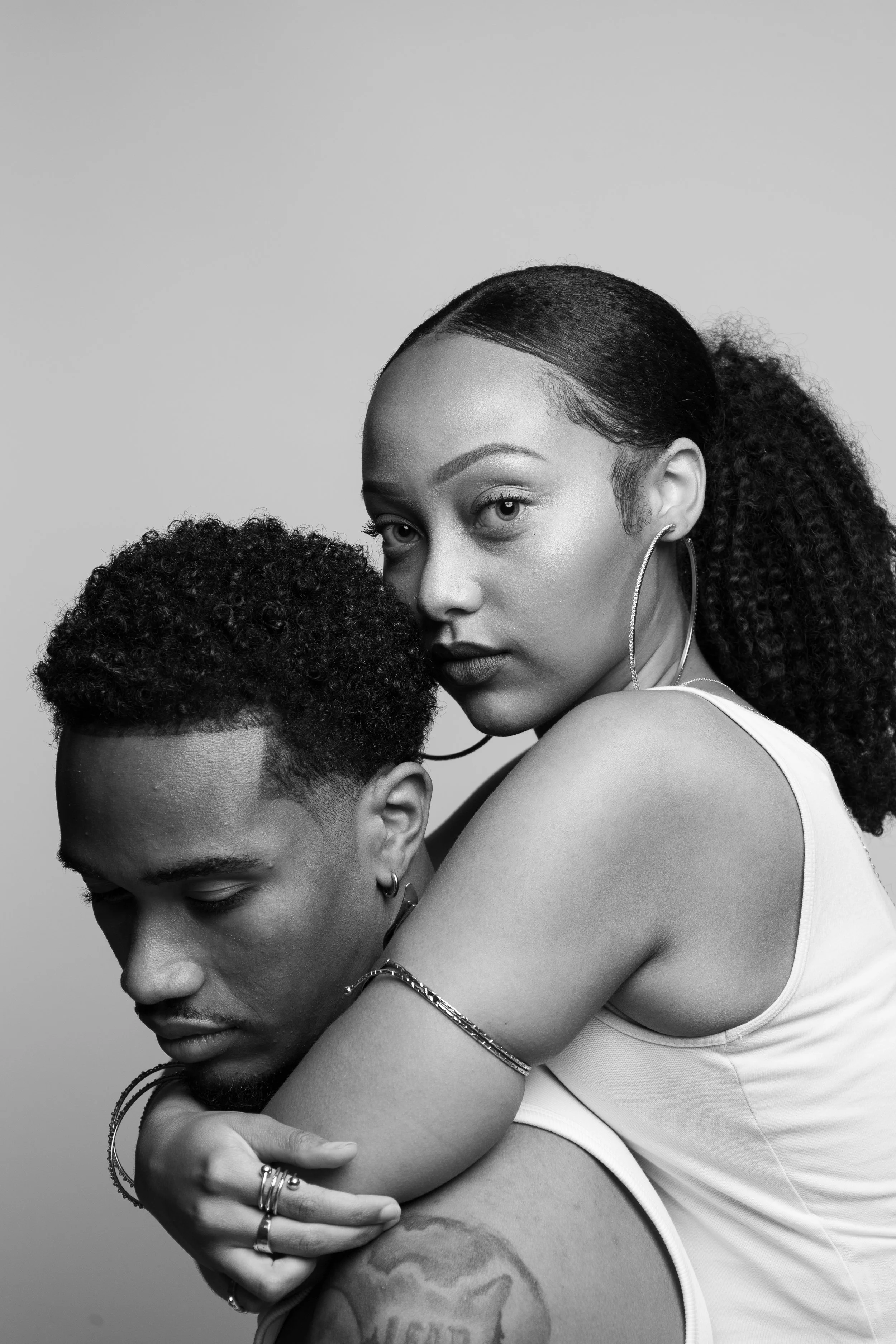 Black and white portrait of a woman embracing a man from behind, both wearing tank tops.