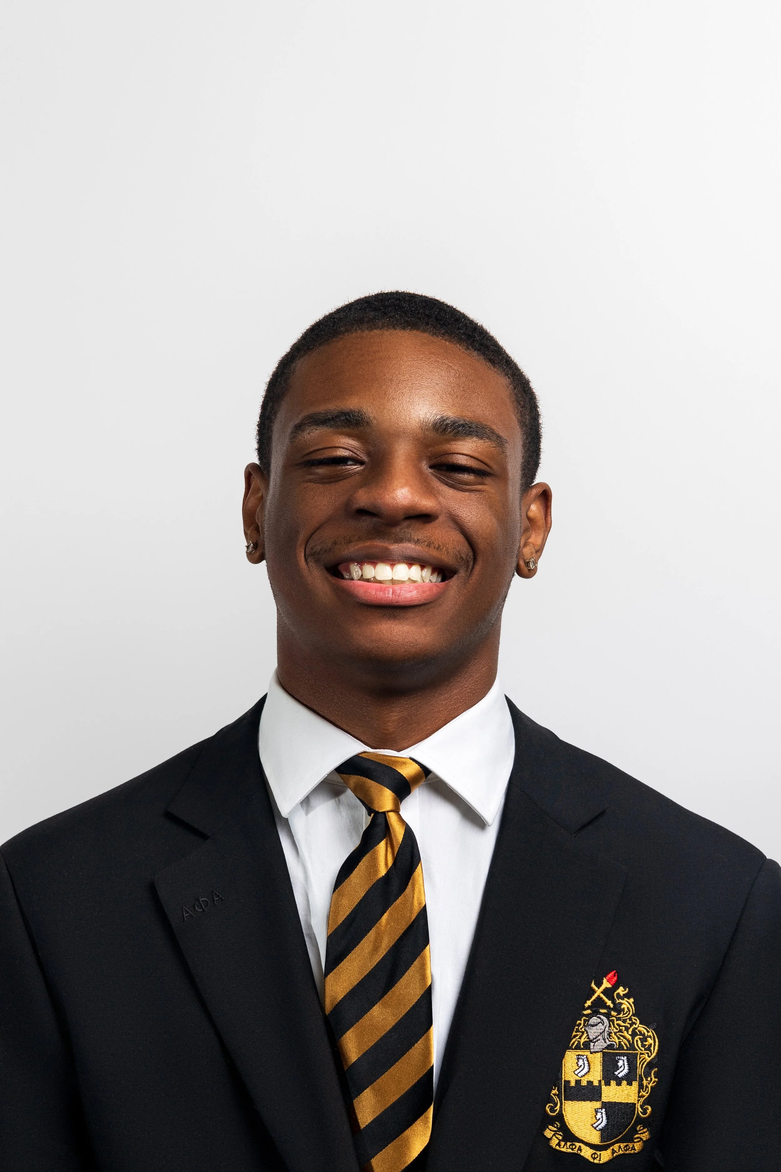 Smiling person in a suit with a striped tie and crest on blazer.
