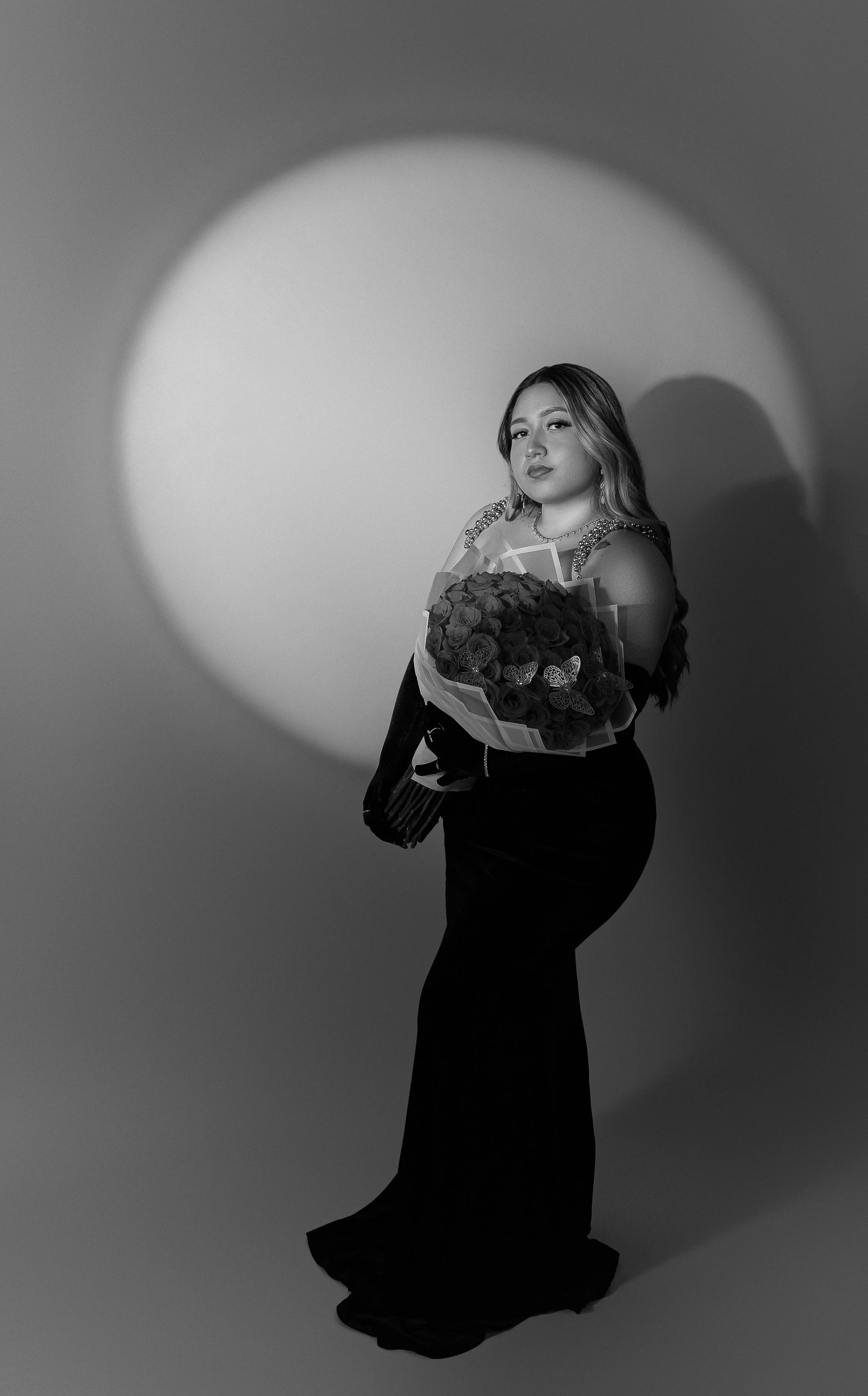 Black and white photo of a woman in an elegant gown holding a bouquet of roses.